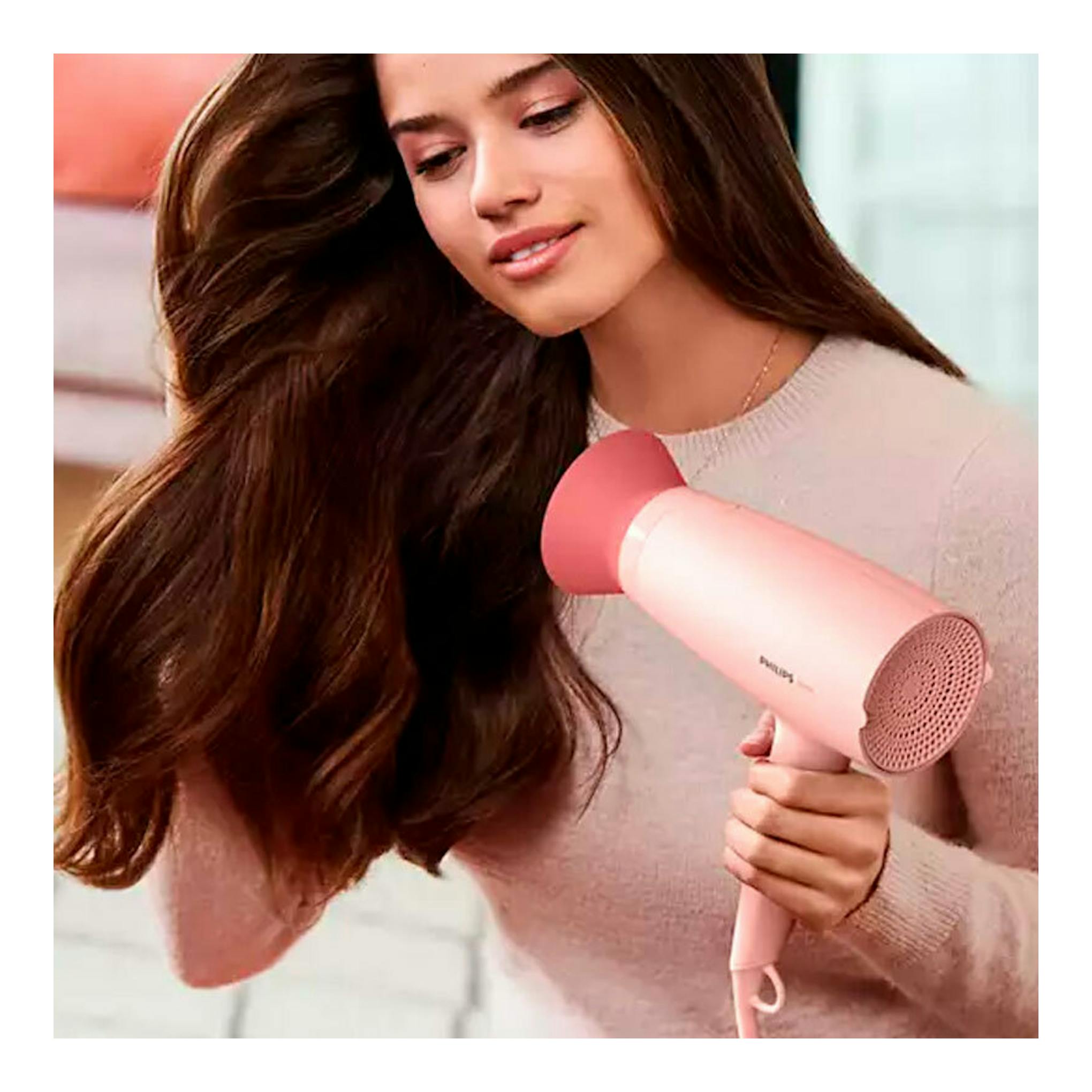Secador de pelo Philips BHP398/00 rosa, en vista frontal, sostenido por una mujer.