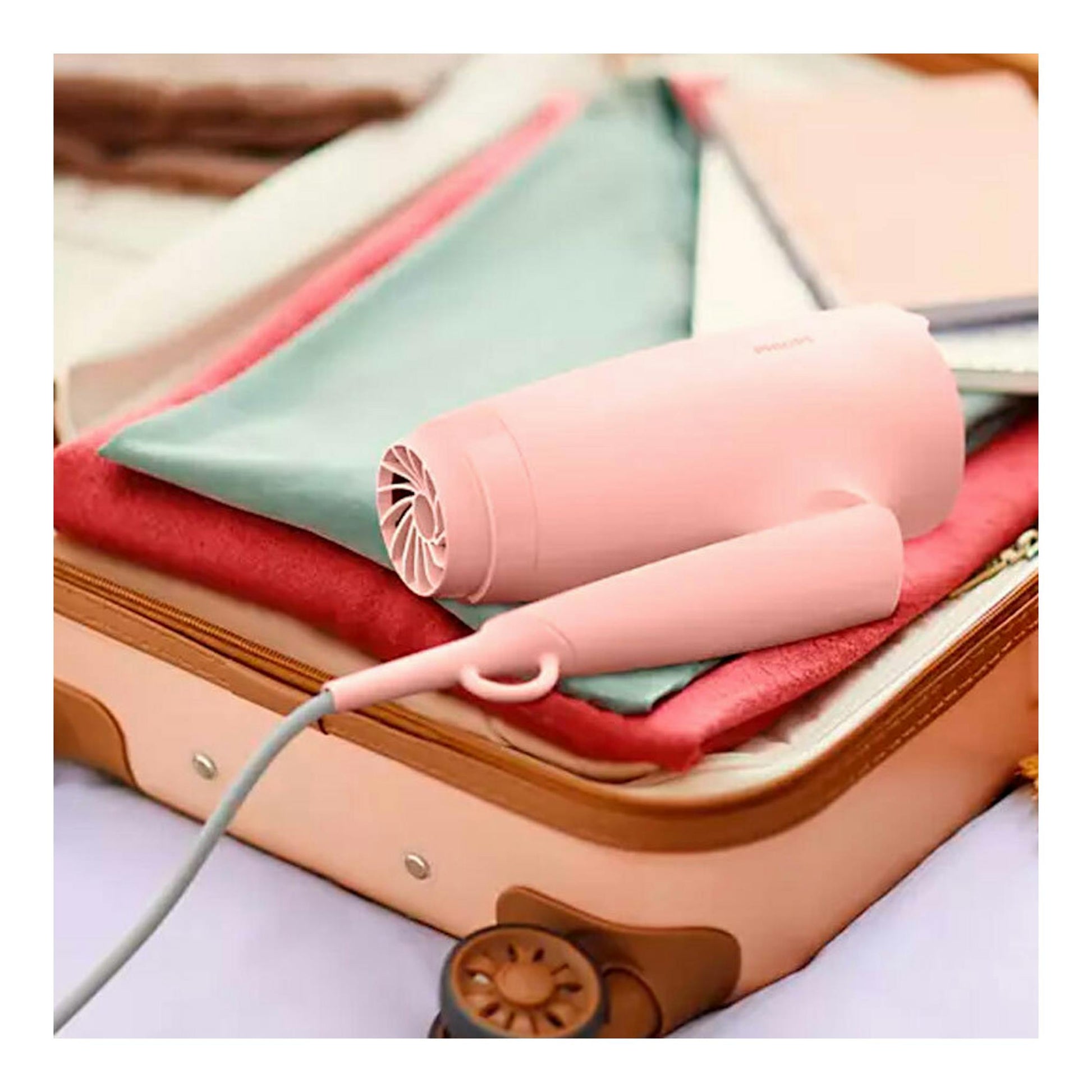 Philips BHP398/00: secador de viaje rosa sobre una maleta abierta con ropa, vista frontal en primer plano.