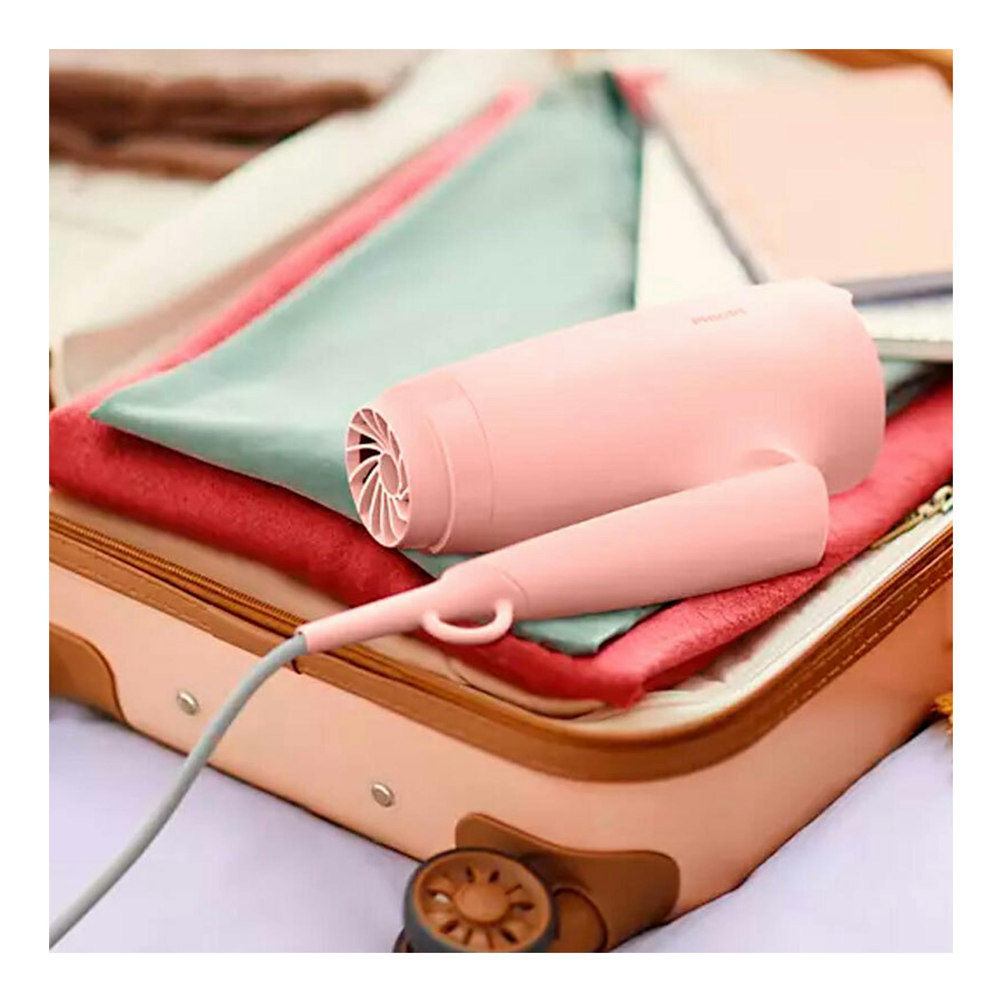 Philips BHP398/00: secador de viaje rosa sobre una maleta abierta con ropa, vista frontal en primer plano.