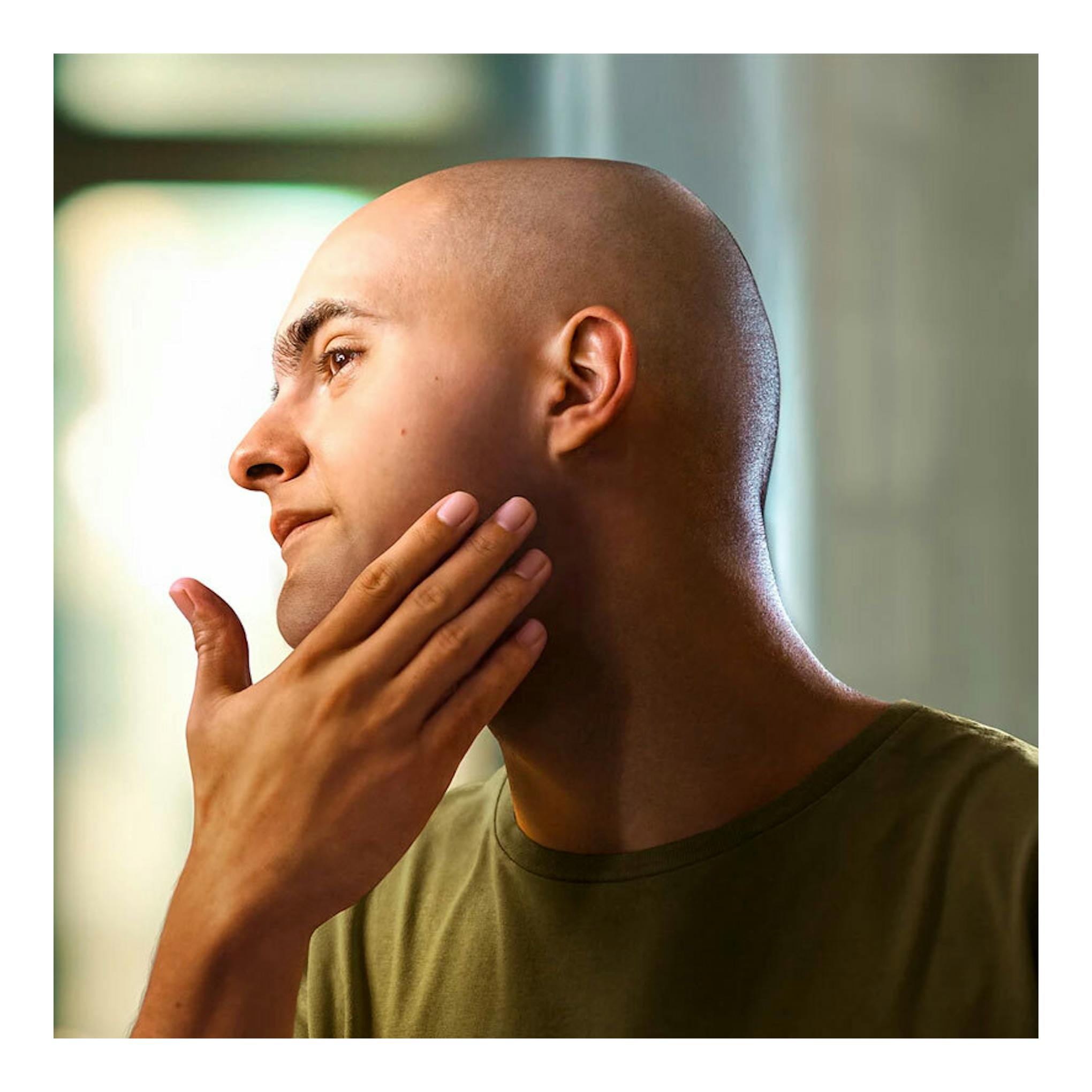 Philips S3143/02: hombre calvo de perfil, tocándose la mandíbula, con camiseta verde.