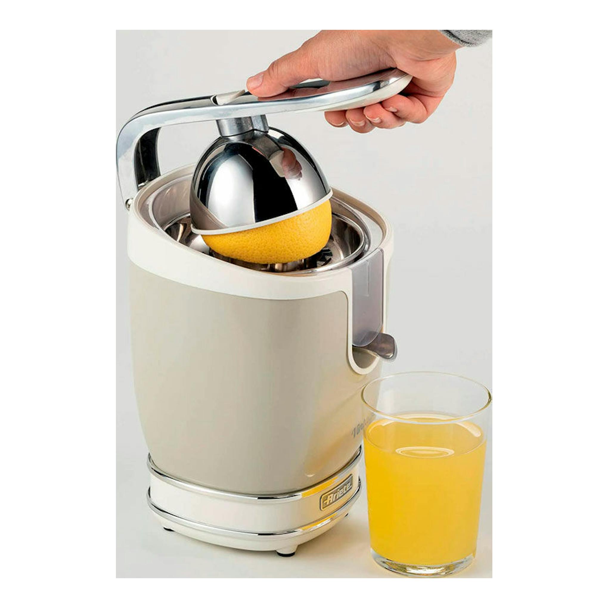 Exprimidor Ariete Vintage 413/03 beige, con una mano presionando un limón y un vaso de zumo al lado.