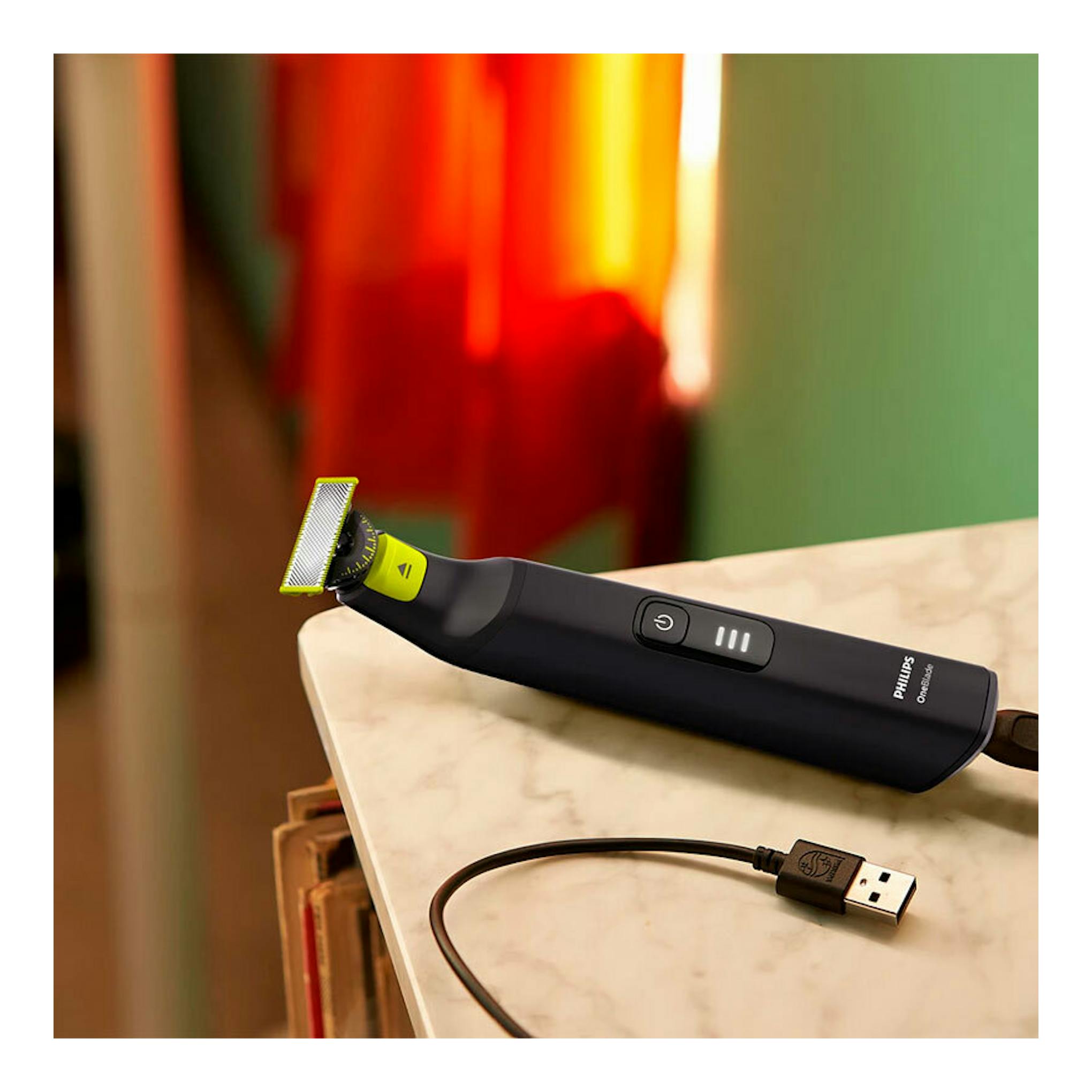 Afeitadora Philips OneBlade QP6542/15 negra, vista lateral sobre una mesa, con cabezal verde y cable USB.