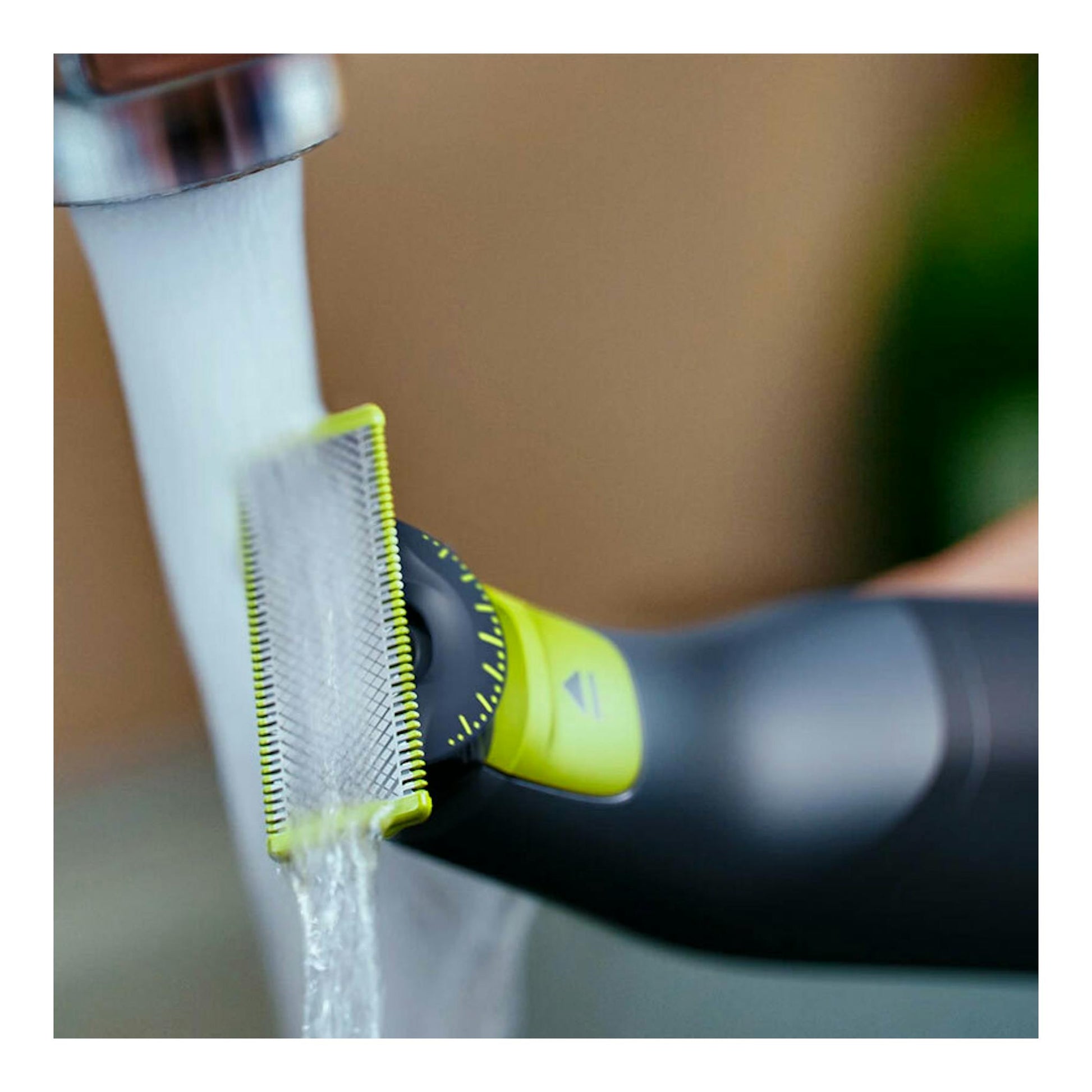 Afeitadora Philips OneBlade QP6542/15 negra y verde, en primer plano, bajo un chorro de agua.
