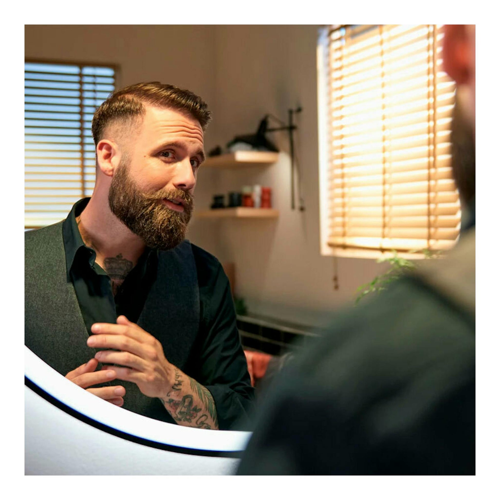 Hombre con barba mirándose en un espejo, en interior, con luz cálida.