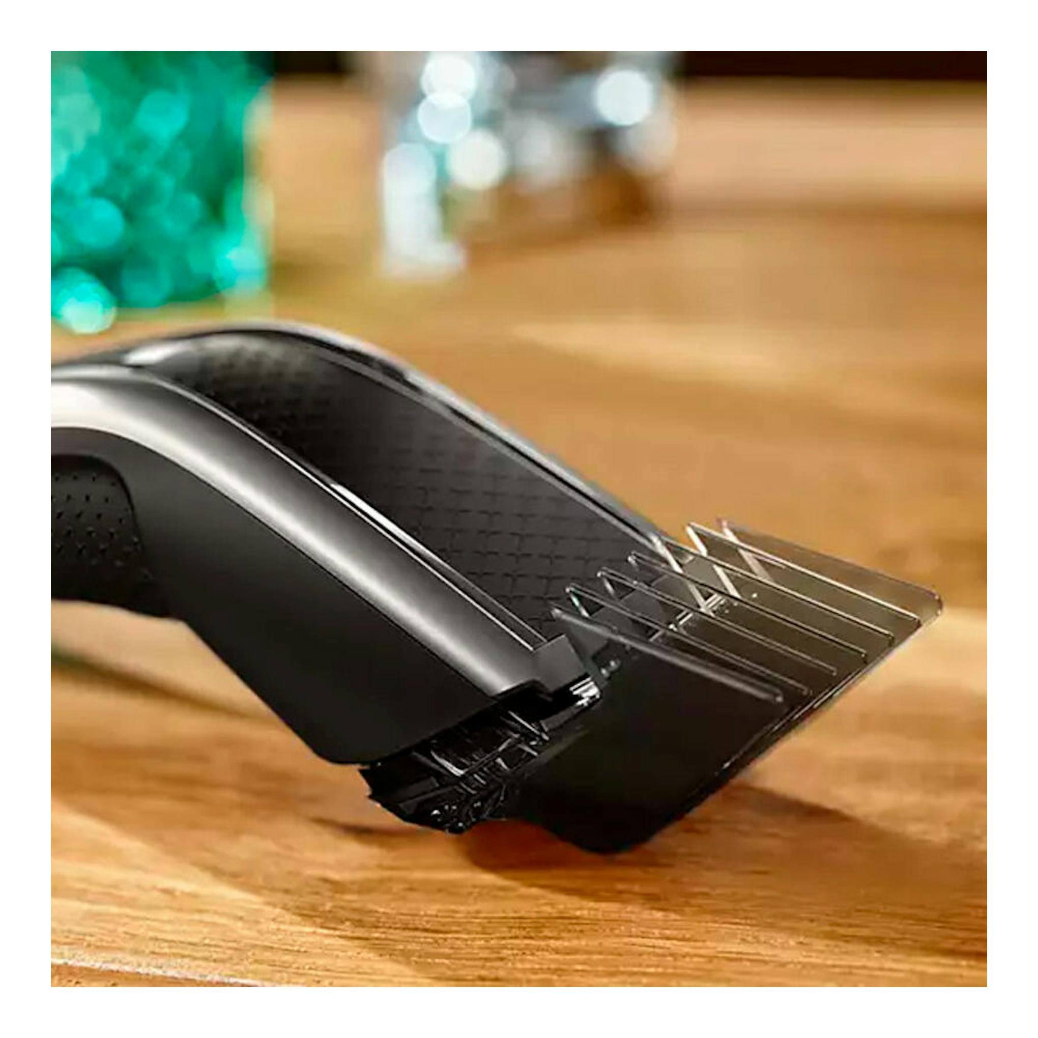 Cortapelo Philips HC5650/15 negro, vista lateral en primer plano, con peine guía sobre superficie de madera.
