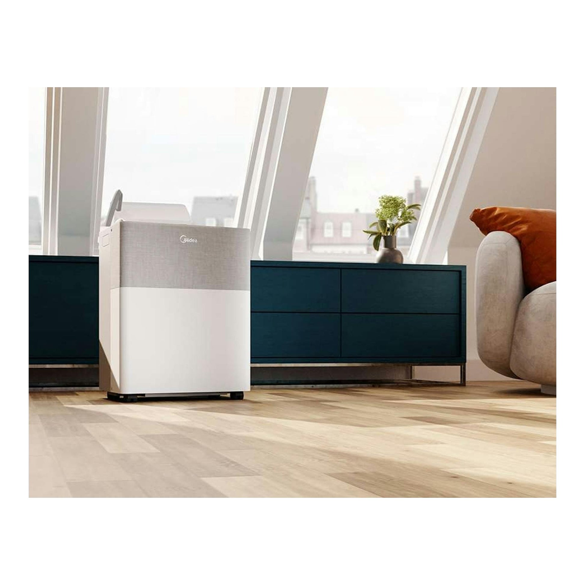 Aire acondicionado portátil Midea blanco y gris, vista frontal en una sala junto a una ventana.