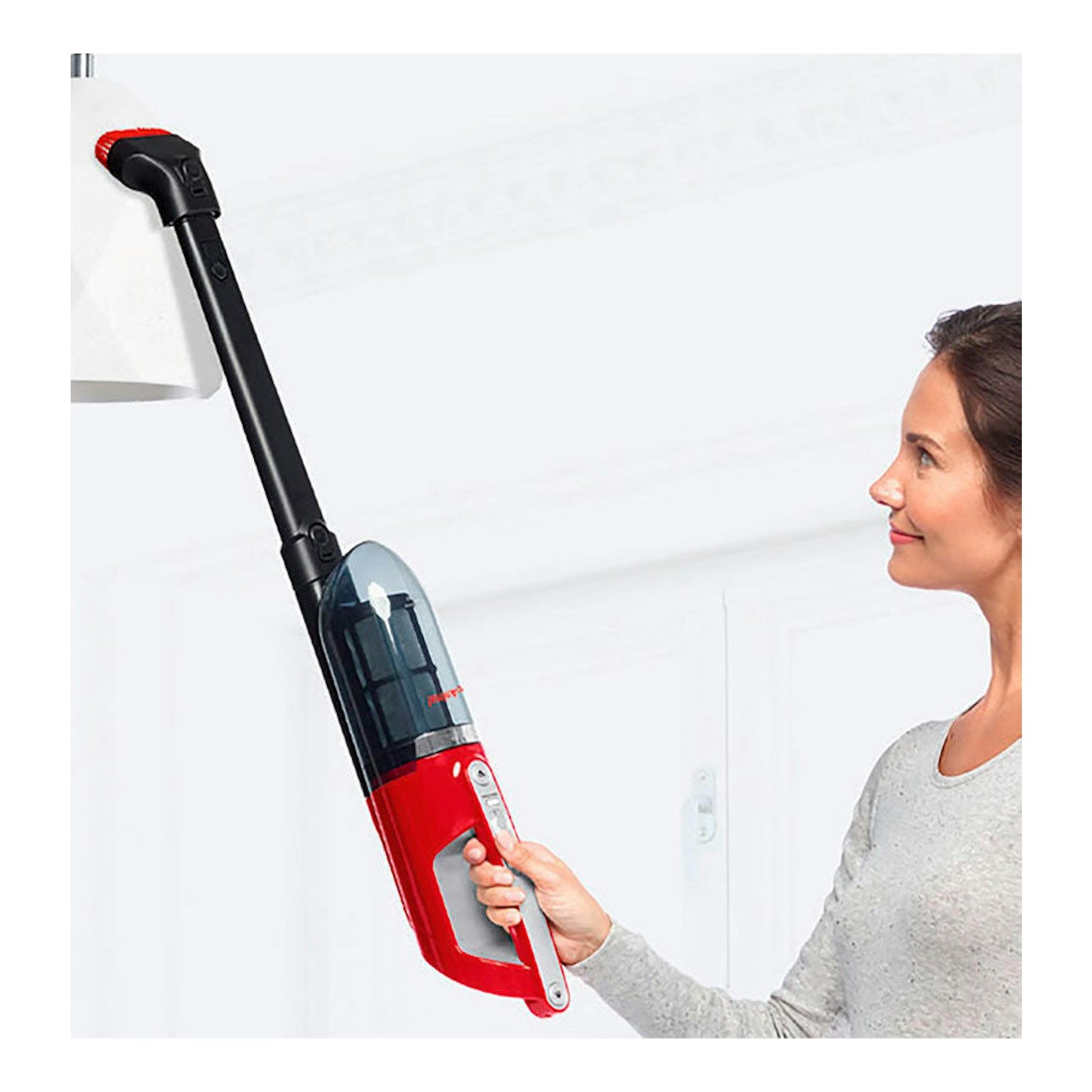 Aspirador escoba Bosch BBH3ZOO25 rojo y negro, visto en vertical, sostenido por una mujer junto a una lámpara.