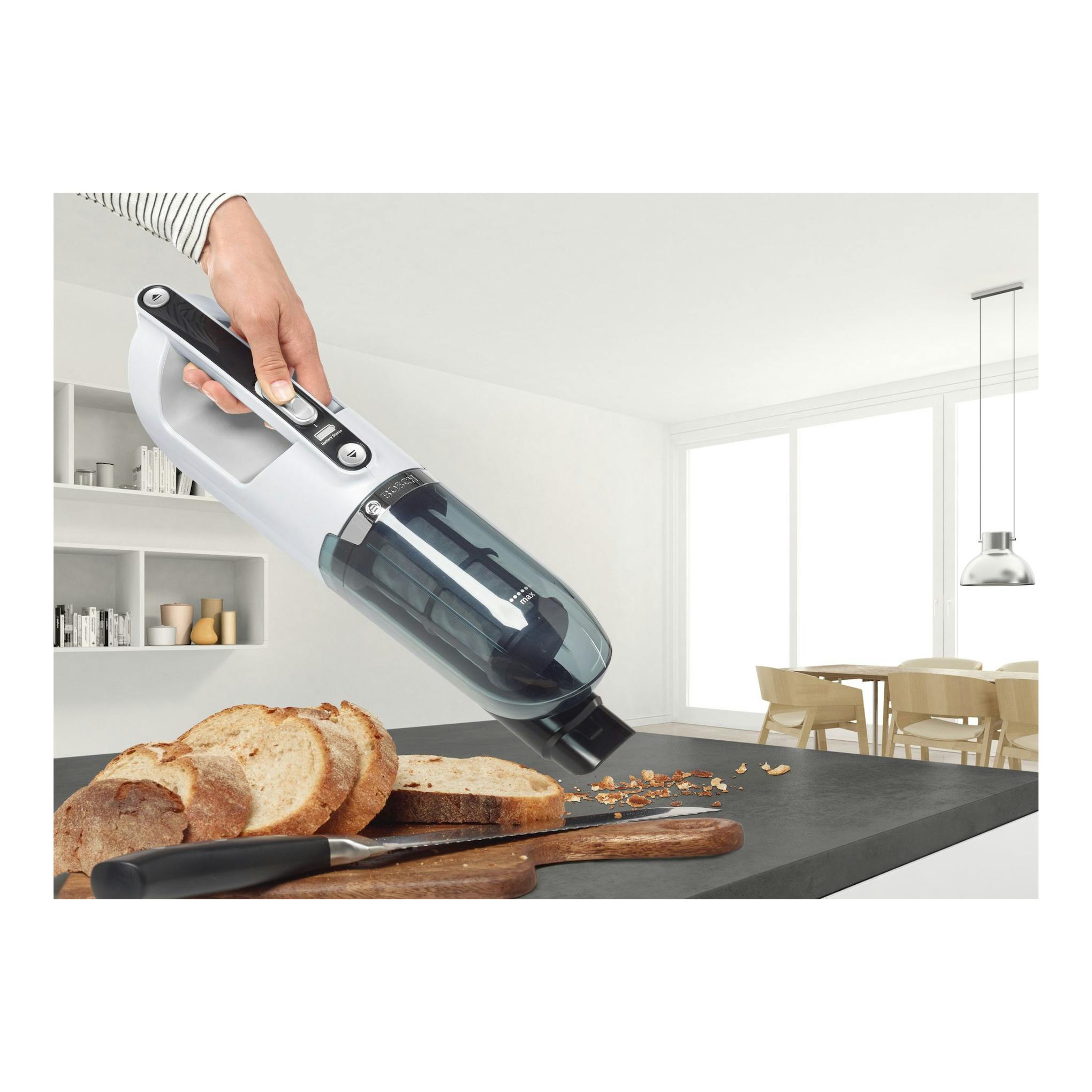 Aspirador escoba Bosch Flexxo BBH32551 blanco y negro, vista lateral, sostenido por una mano sobre migas.