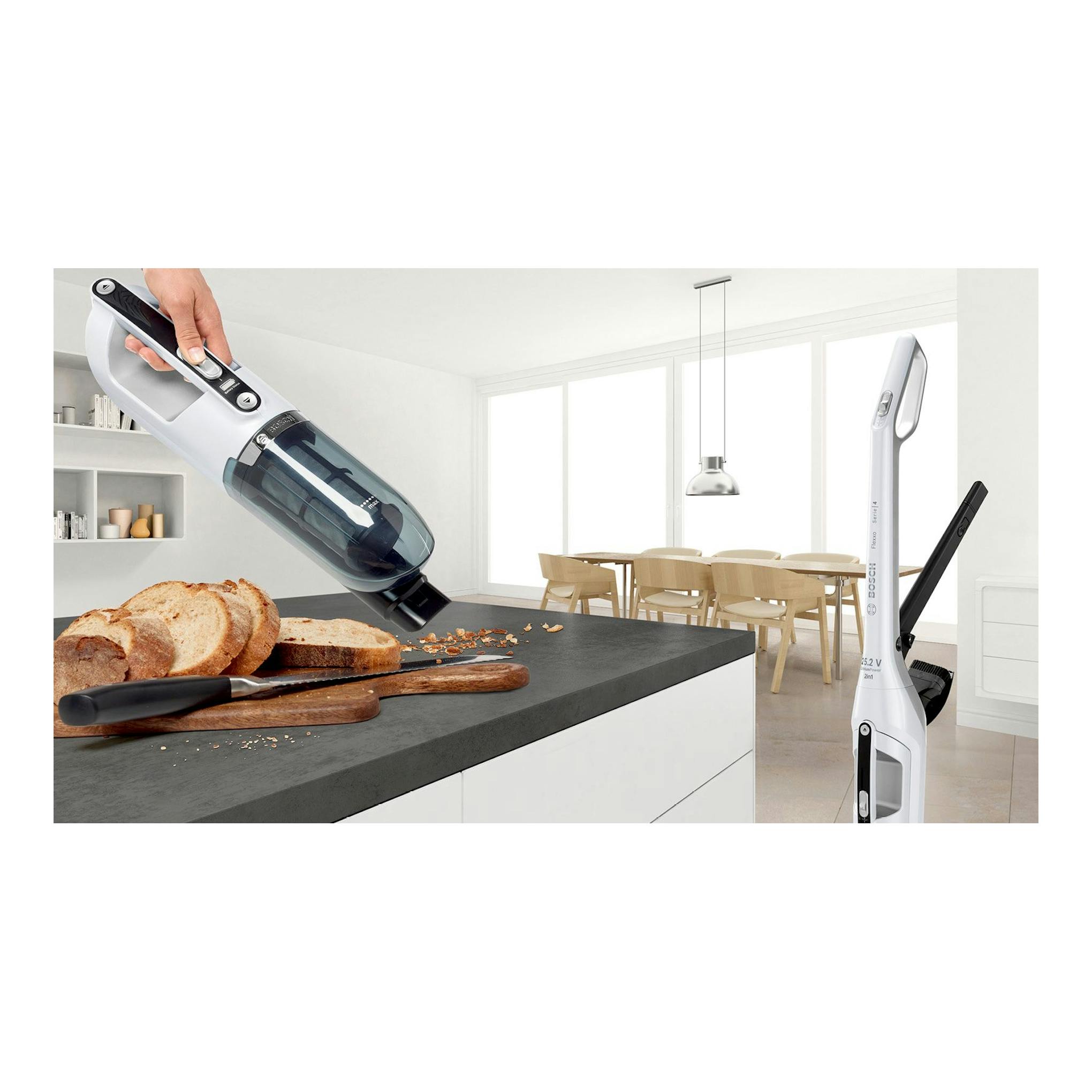 Aspirador escoba Bosch Flexxo BBH32551 blanco, sin cable, en cocina, recogiendo migas sobre una encimera.