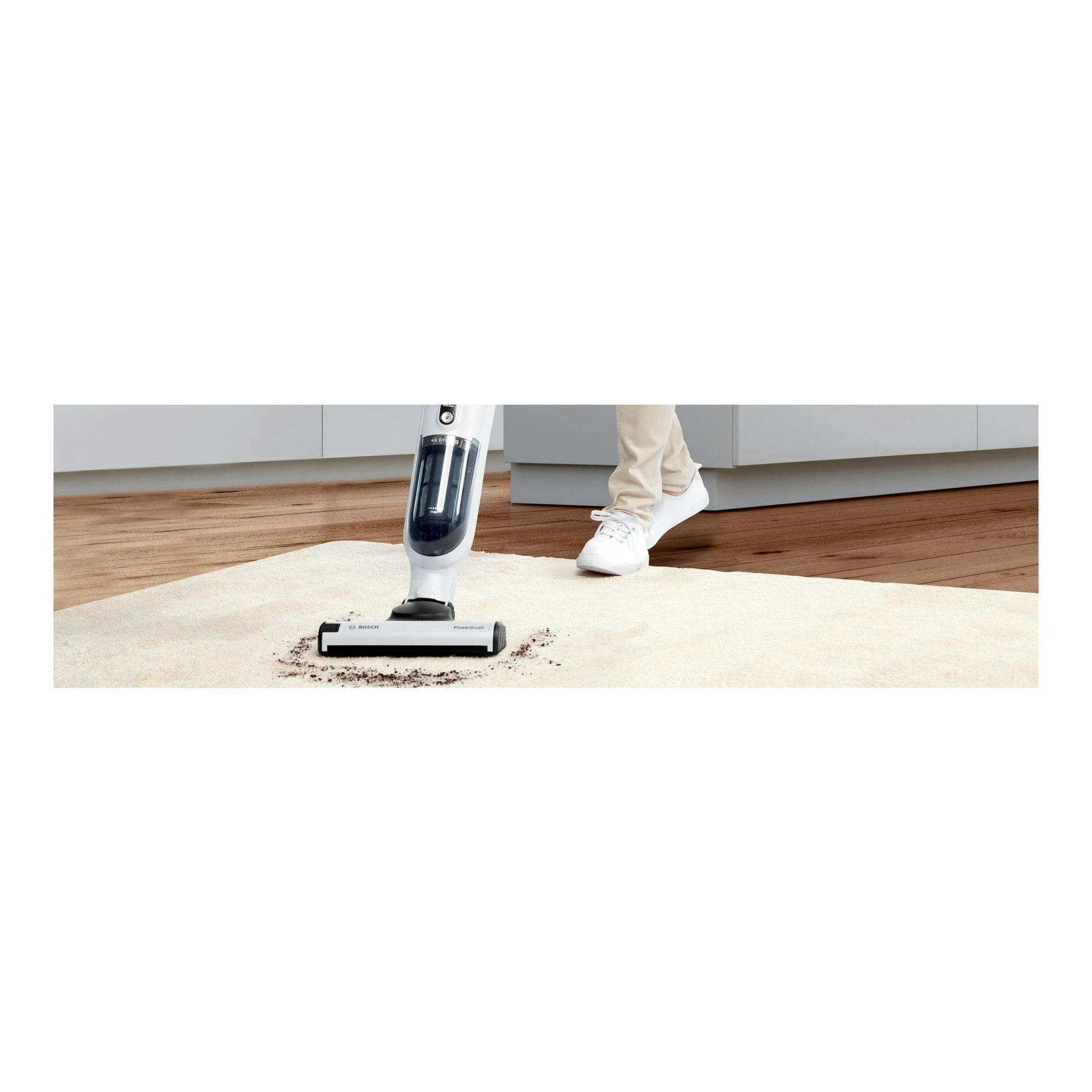 Vista frontal de aspirador escoba Bosch Flexxo BBH32551 blanco sobre una alfombra, con una persona al lado.