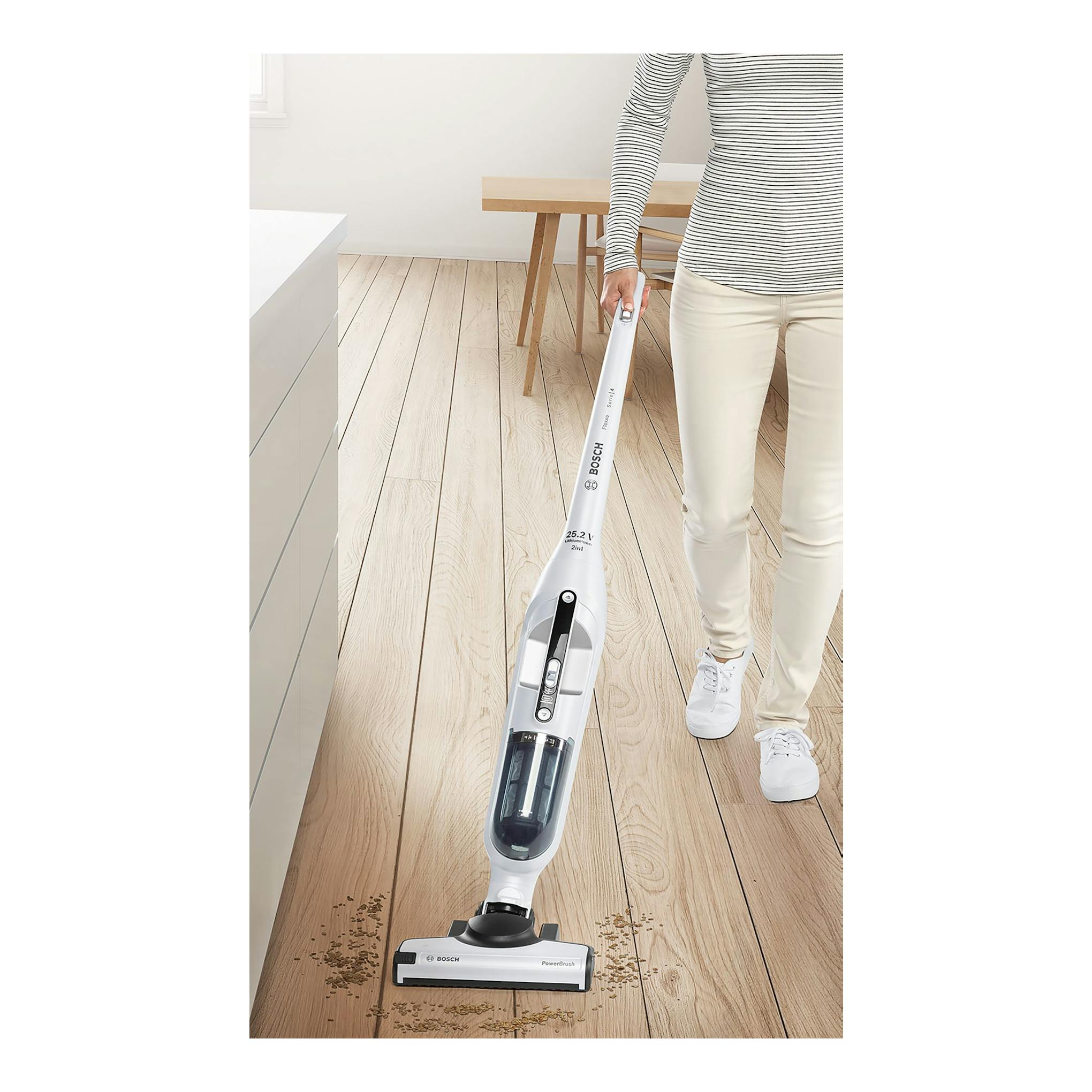 Aspirador escoba Bosch Flexxo BBH32551 blanco, en uso sobre suelo de madera por una persona.