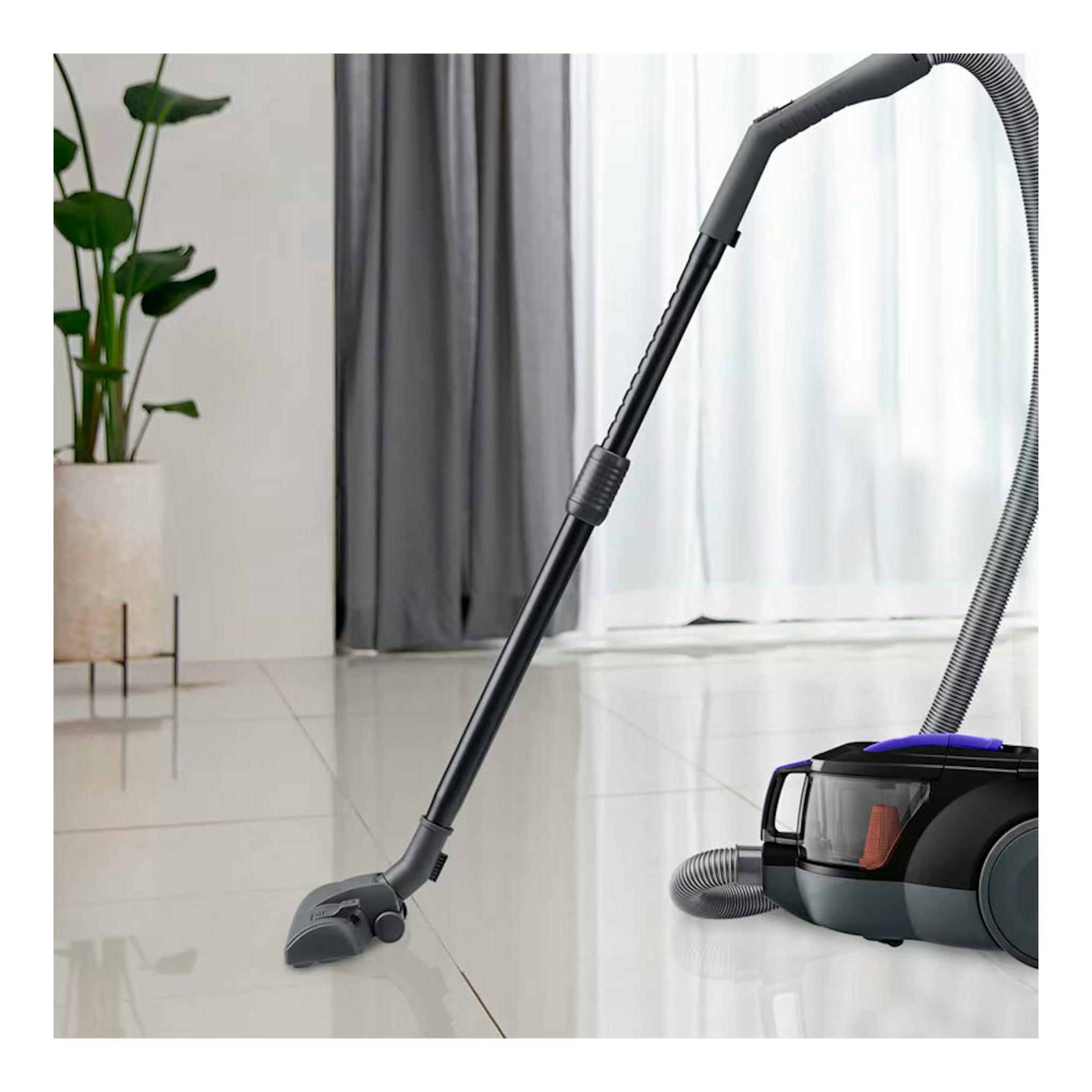 Aspirador LG VC5506NHTB gris mate, vista lateral con tubo y boquilla sobre suelo de baldosas.