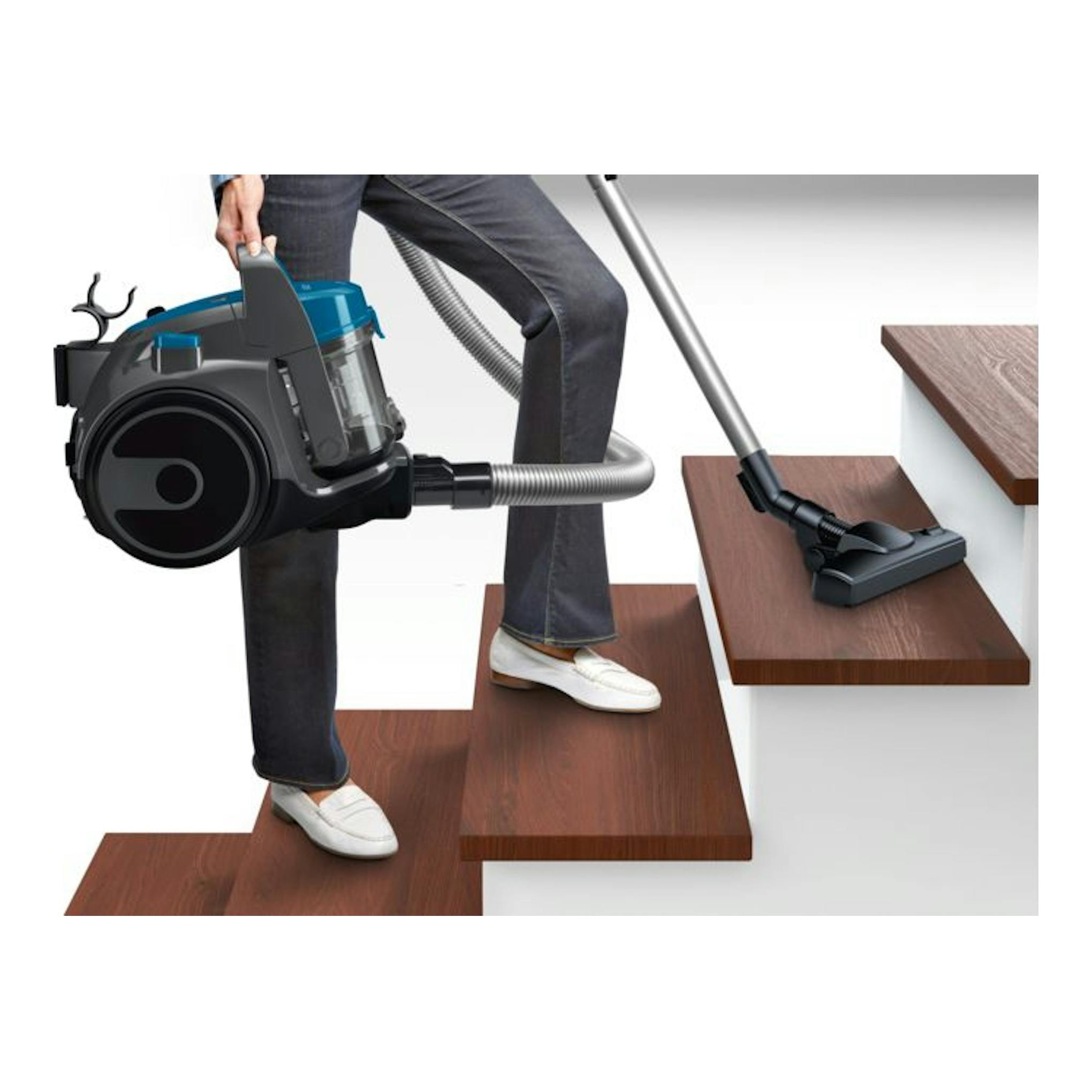 Aspirador sin bolsa Bosch BGS05A220 negro y azul con tubo, sobre escalones de madera.
