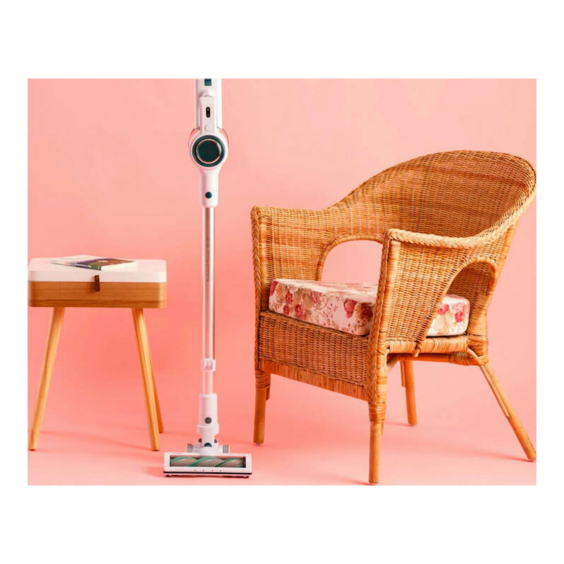 Aspirador vertical Solac AE2505 blanco, de pie sobre fondo rosa, junto a una silla de mimbre y una mesa auxiliar.