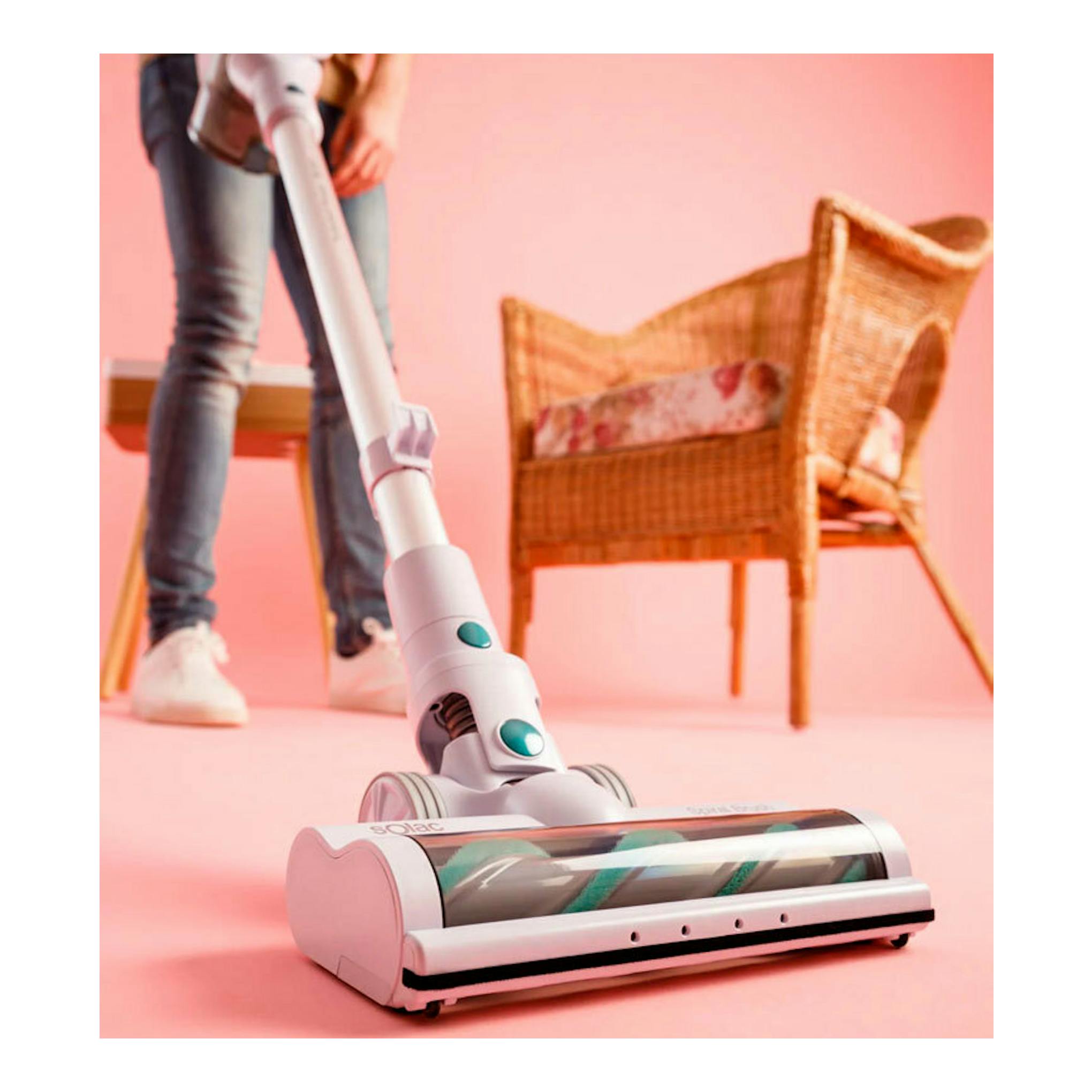 Aspirador Solac AE2505 blanco, en vista frontal baja, usado por una persona sobre suelo rosa.