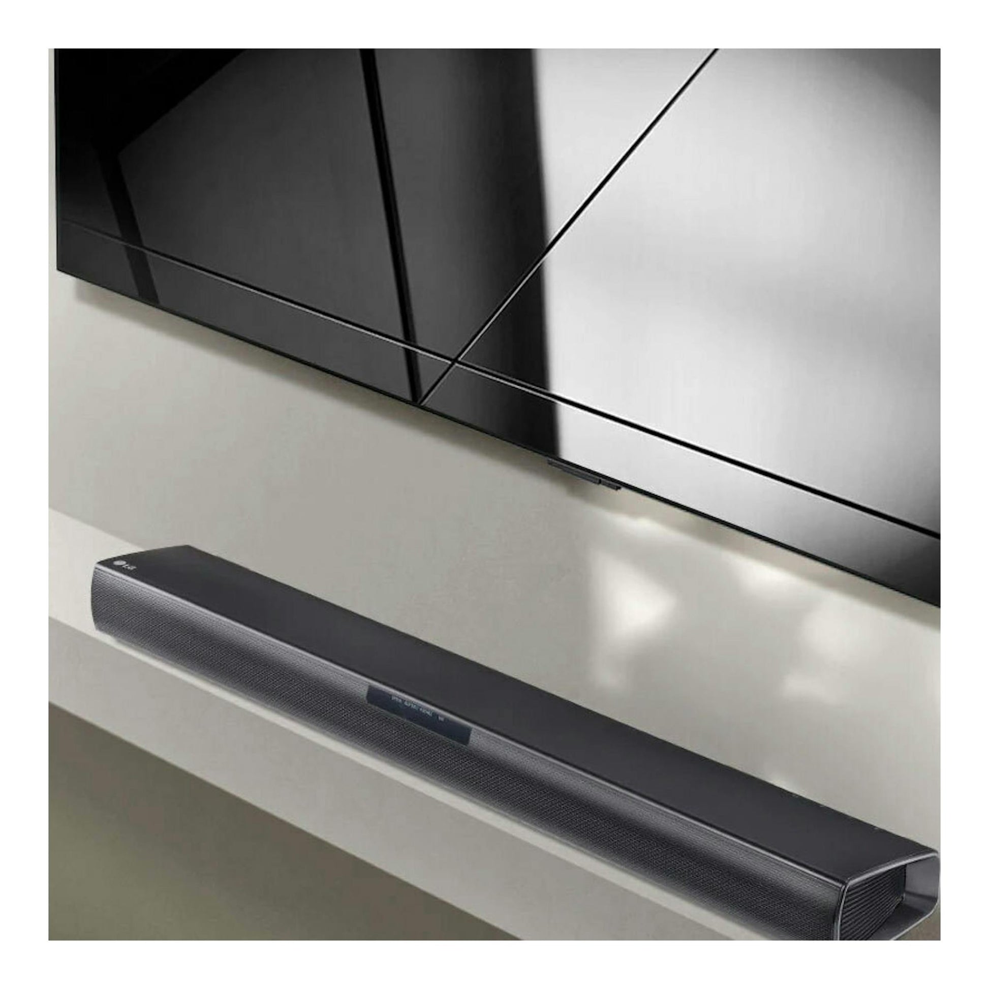 Barra de sonido LG SQC1 negra, vista en ángulo bajo, colocada bajo un televisor montado en pared.