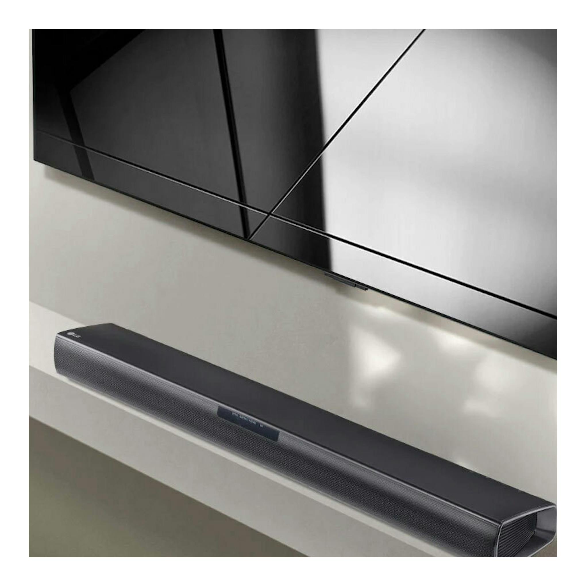 Barra de sonido LG SQC1 negra, vista en ángulo bajo, colocada bajo un televisor montado en pared.