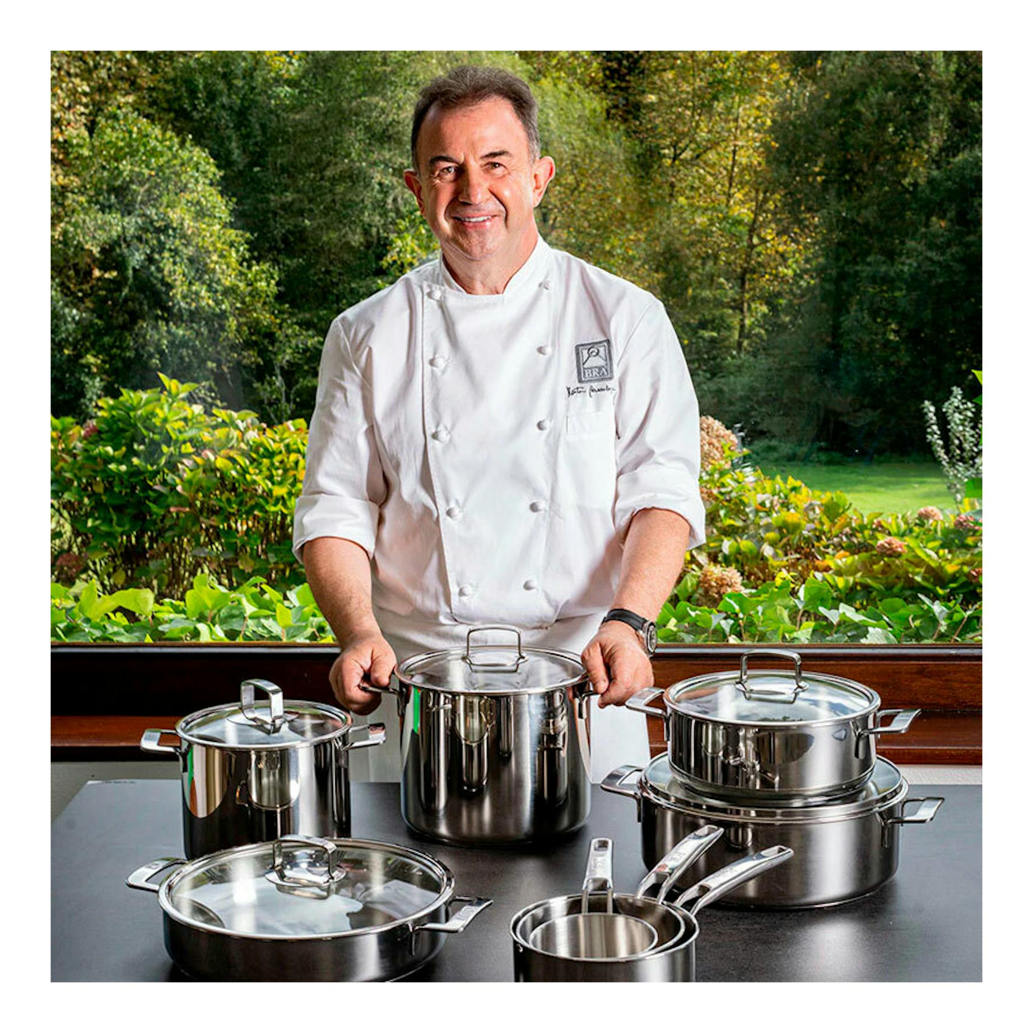 Vista frontal de un chef con batería de cocina BRA Signature de acero inoxidable, 7 piezas, sobre una mesa.