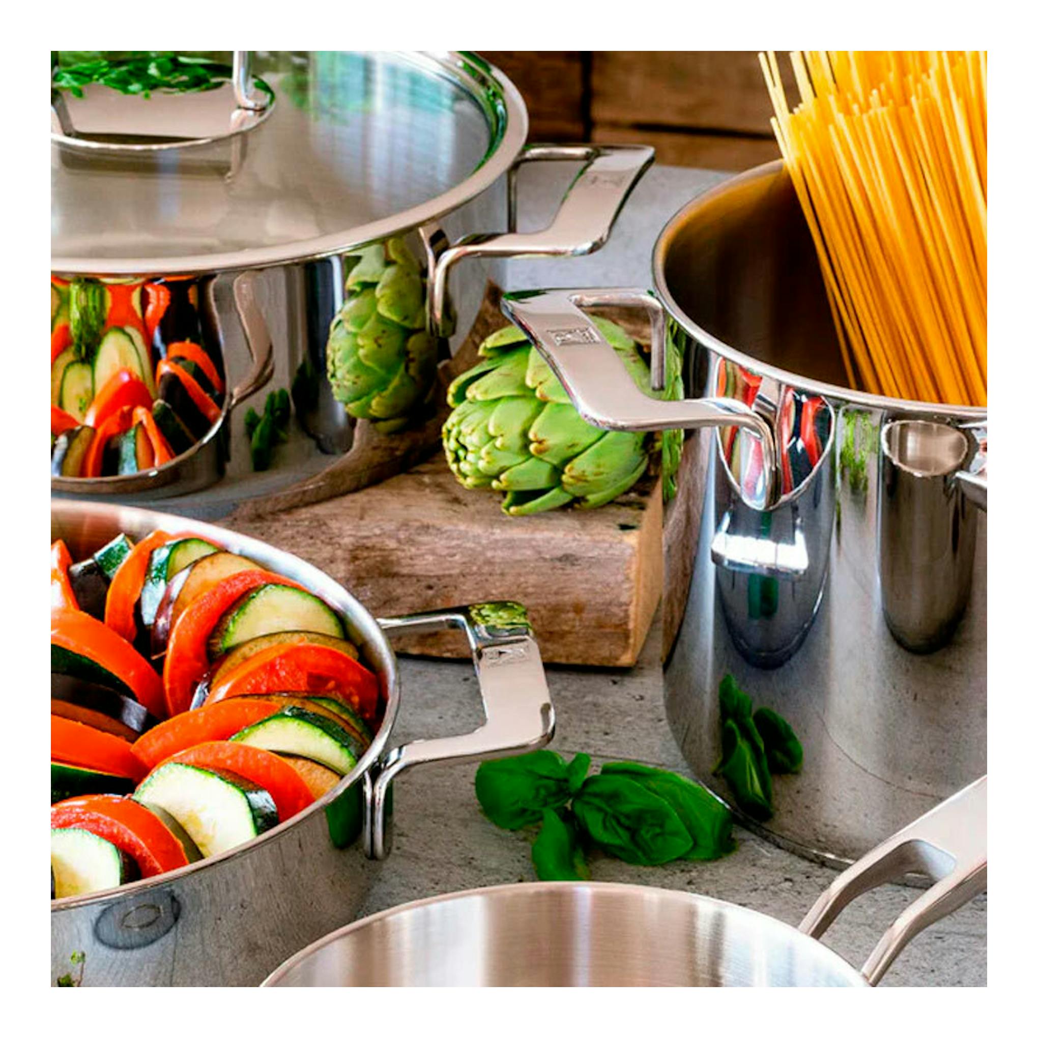 Batería de cocina Bra Signature de acero inoxidable, varias ollas vistas desde arriba con pasta y verduras.