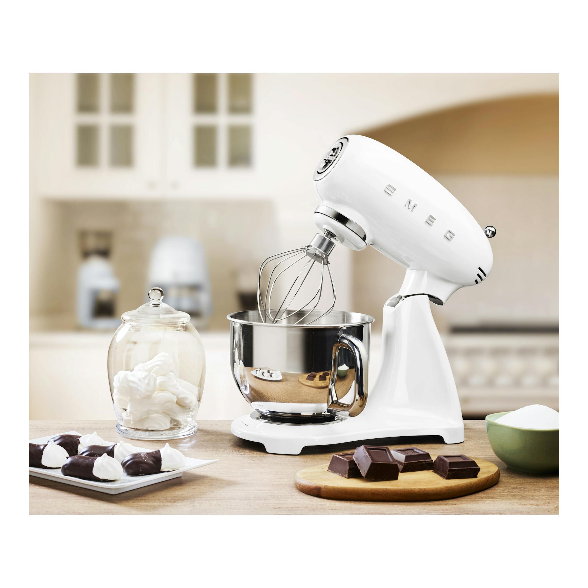 Batidora amasadora Smeg SMF03WHEU blanca, vista lateral, con bol de acero y varillas sobre encimera.