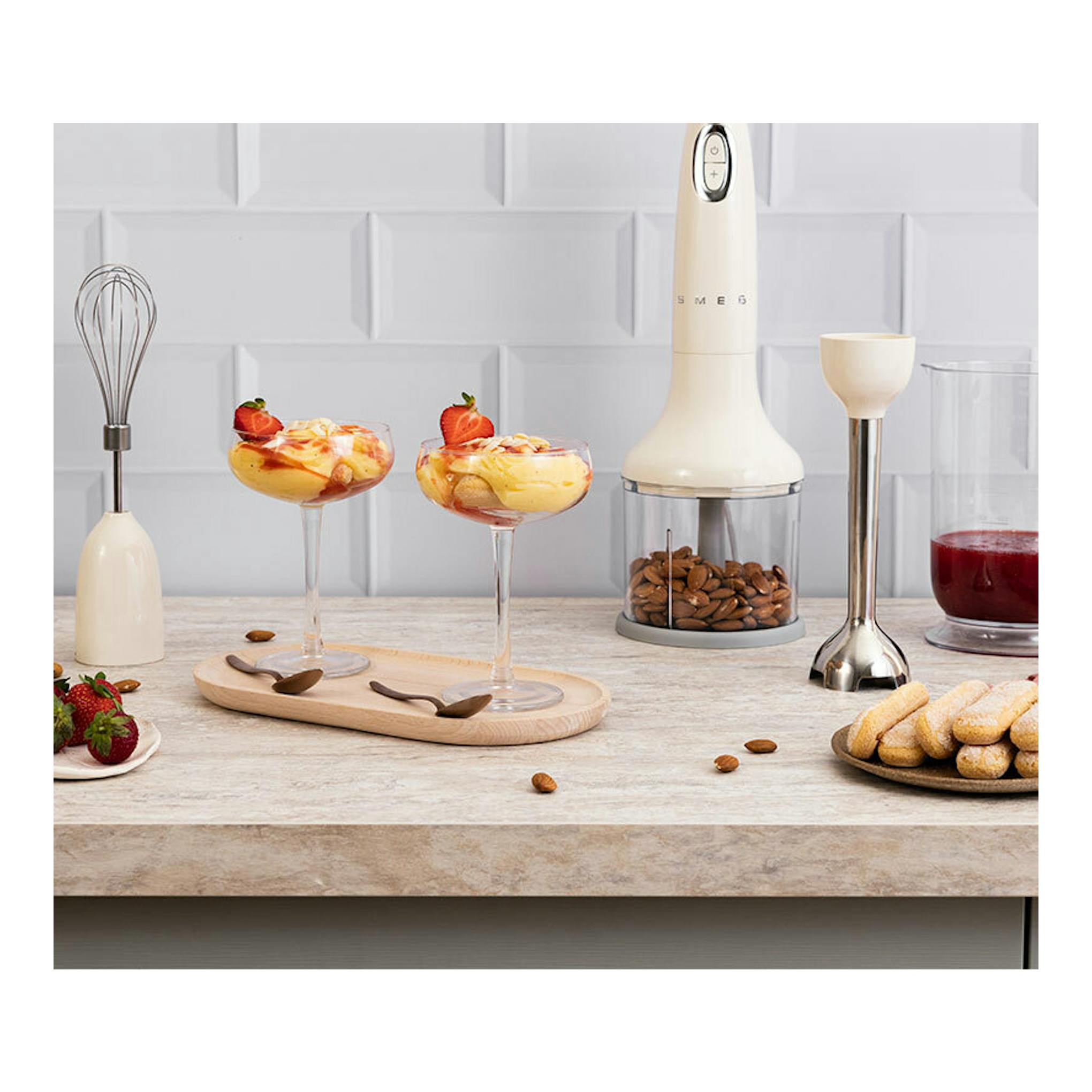 Batidora de mano Smeg HBF03CREU crema, vista frontal, con accesorios sobre una encimera de cocina.