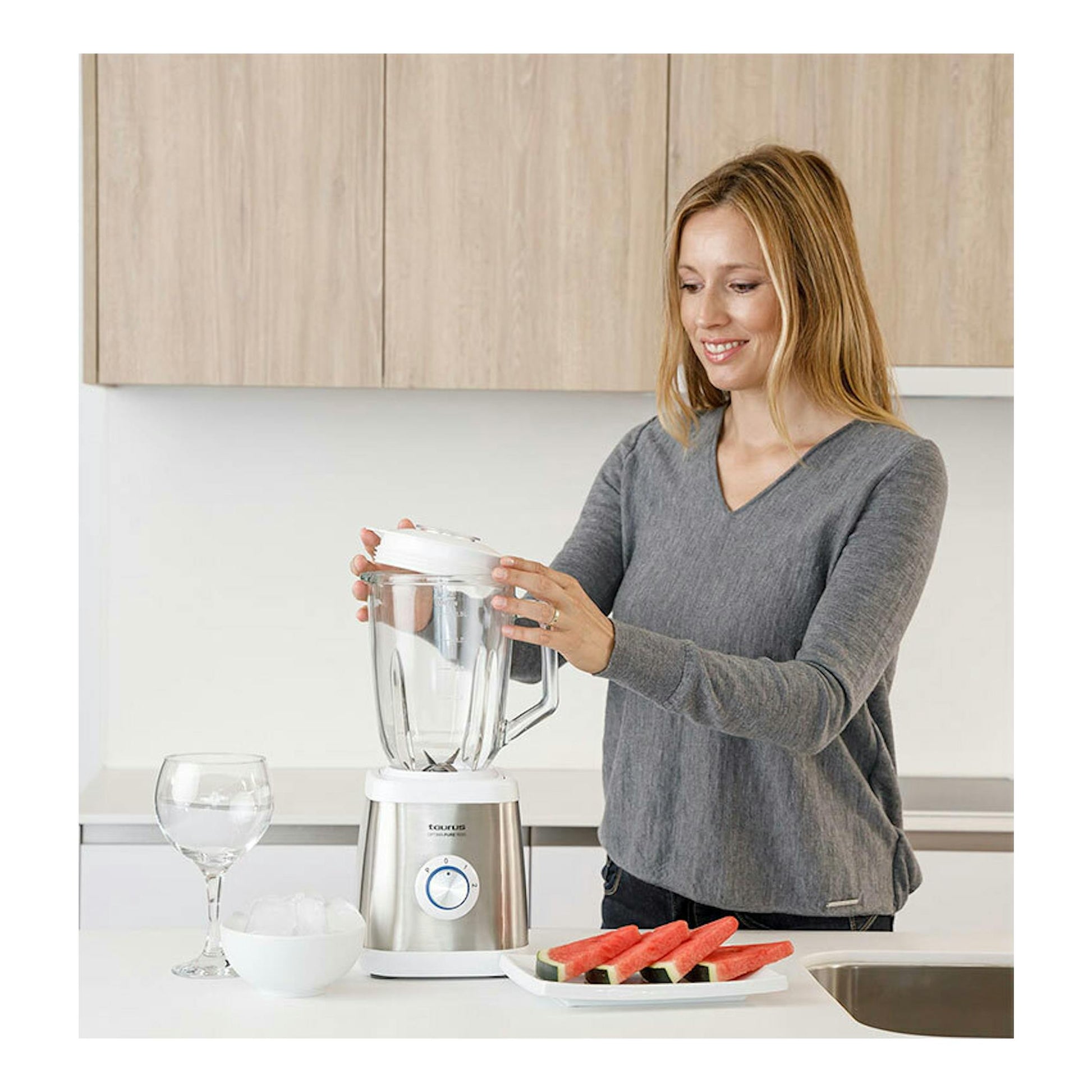Batidora de vaso Taurus Optima Pure 1500 blanca y acero inoxidable sobre encimera, con una mujer colocándole la tapa.