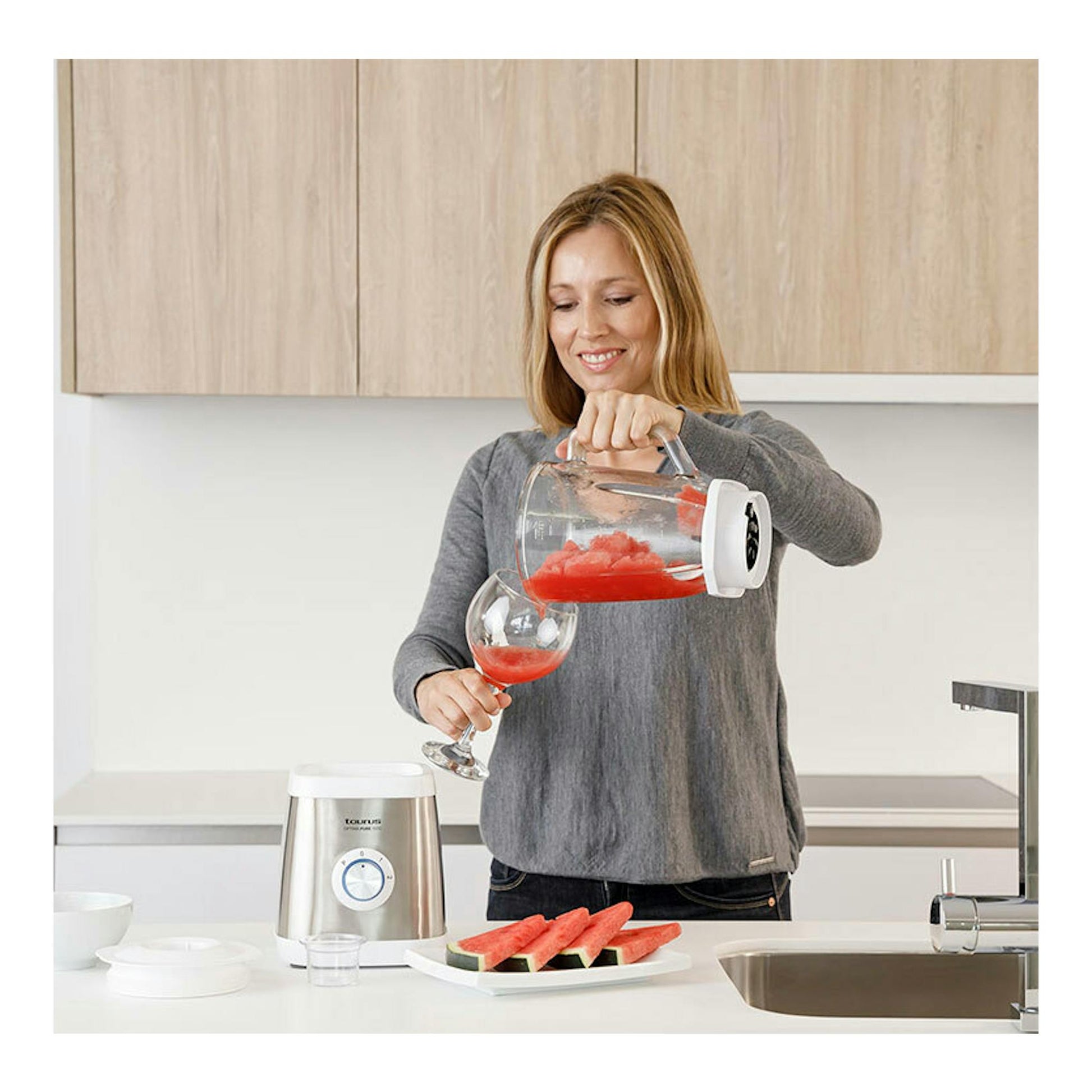 Batidora de vaso Taurus Optima Pure 1500 plateada en cocina, con una mujer sirviendo batido rojo.