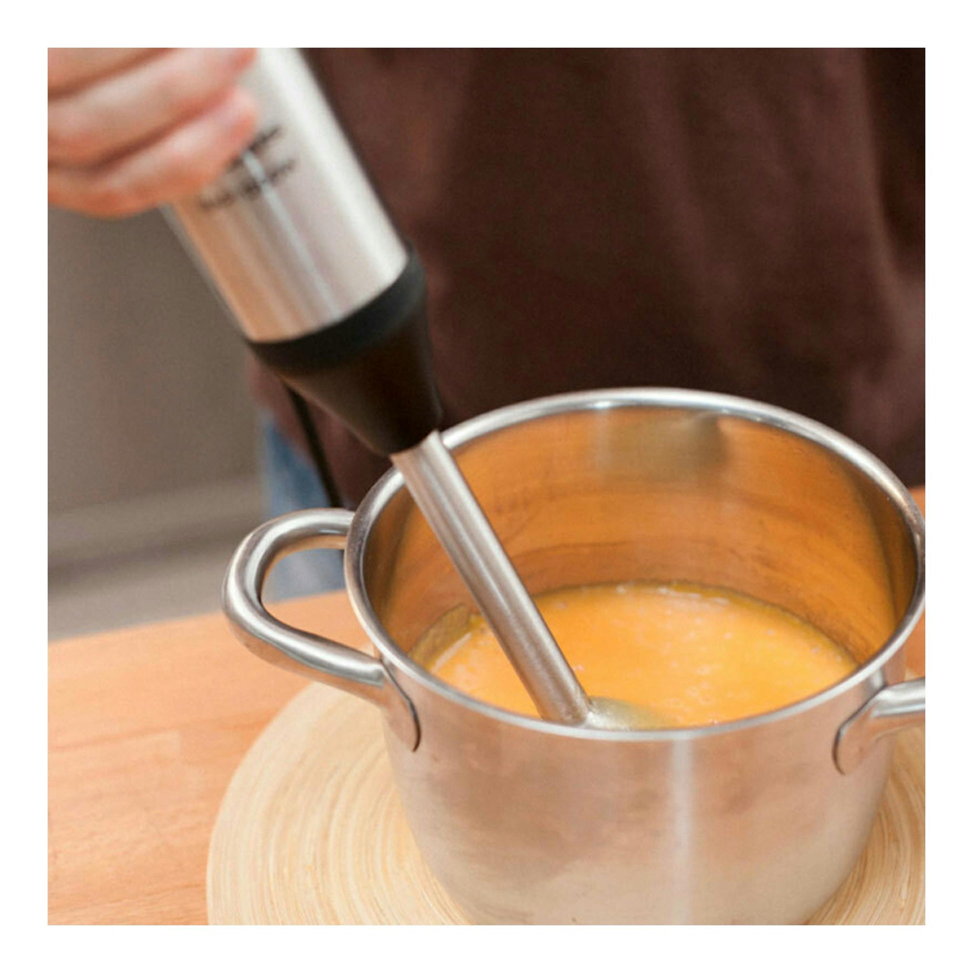 Batidora de mano Taurus Bapi 1200 Inox batiendo crema naranja en una olla de acero inoxidable.
