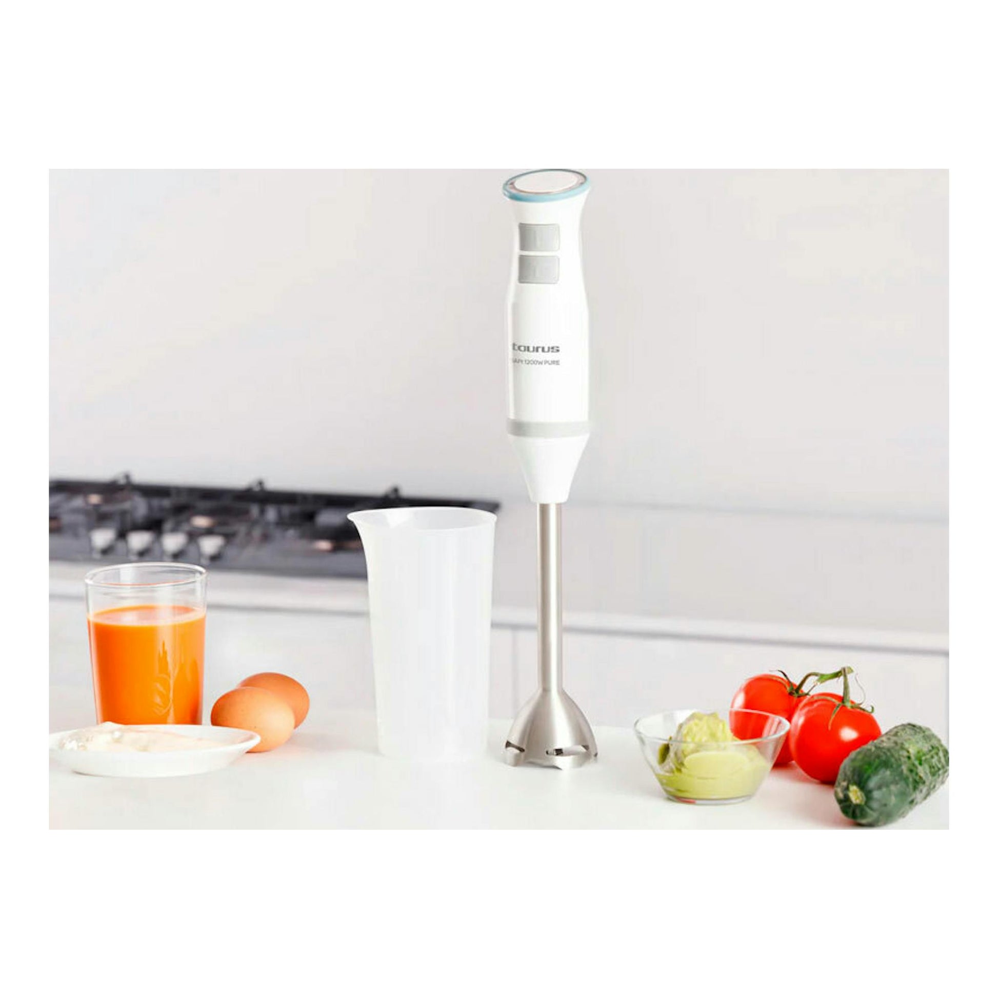 Batidora de mano Taurus Bapi 1200 Pure blanca, vista frontal, con vaso y alimentos sobre una encimera de cocina.