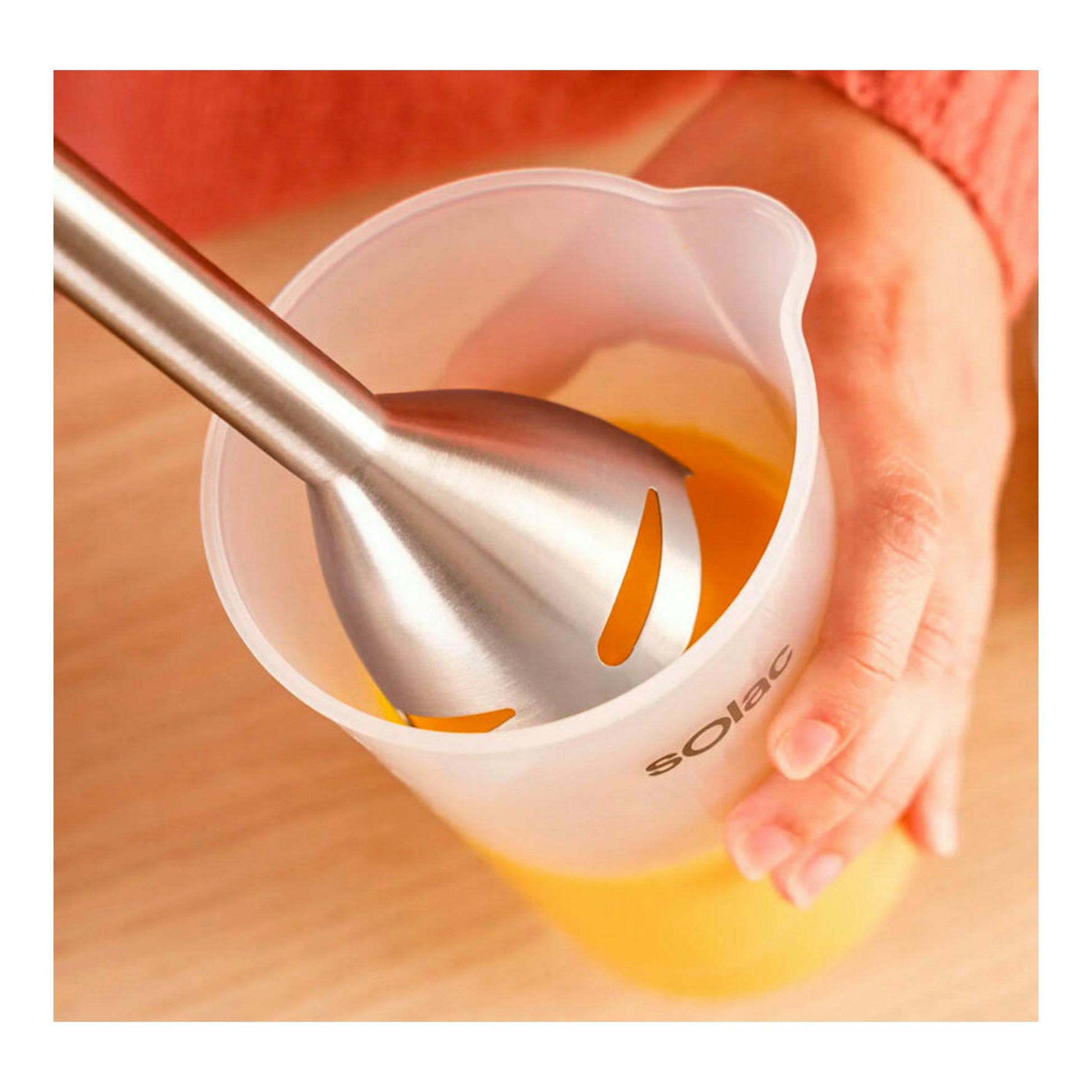 Batidora de mano Solac BA5617 de acero, en vaso medidor translúcido con líquido amarillo, vista cenital.