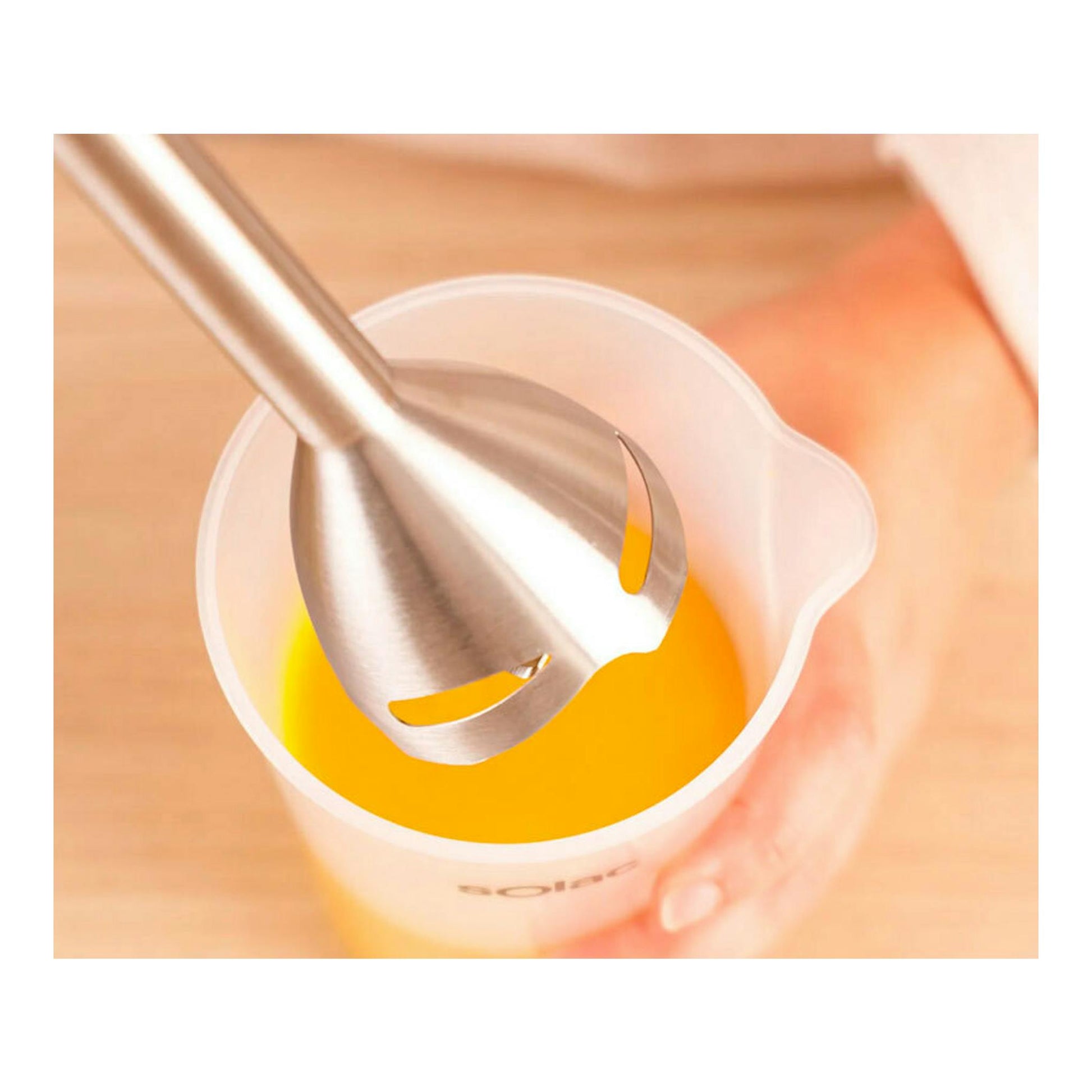 Batidora de mano Solac BA5618, vista cenital, mezclando líquido naranja en un vaso medidor blanco.