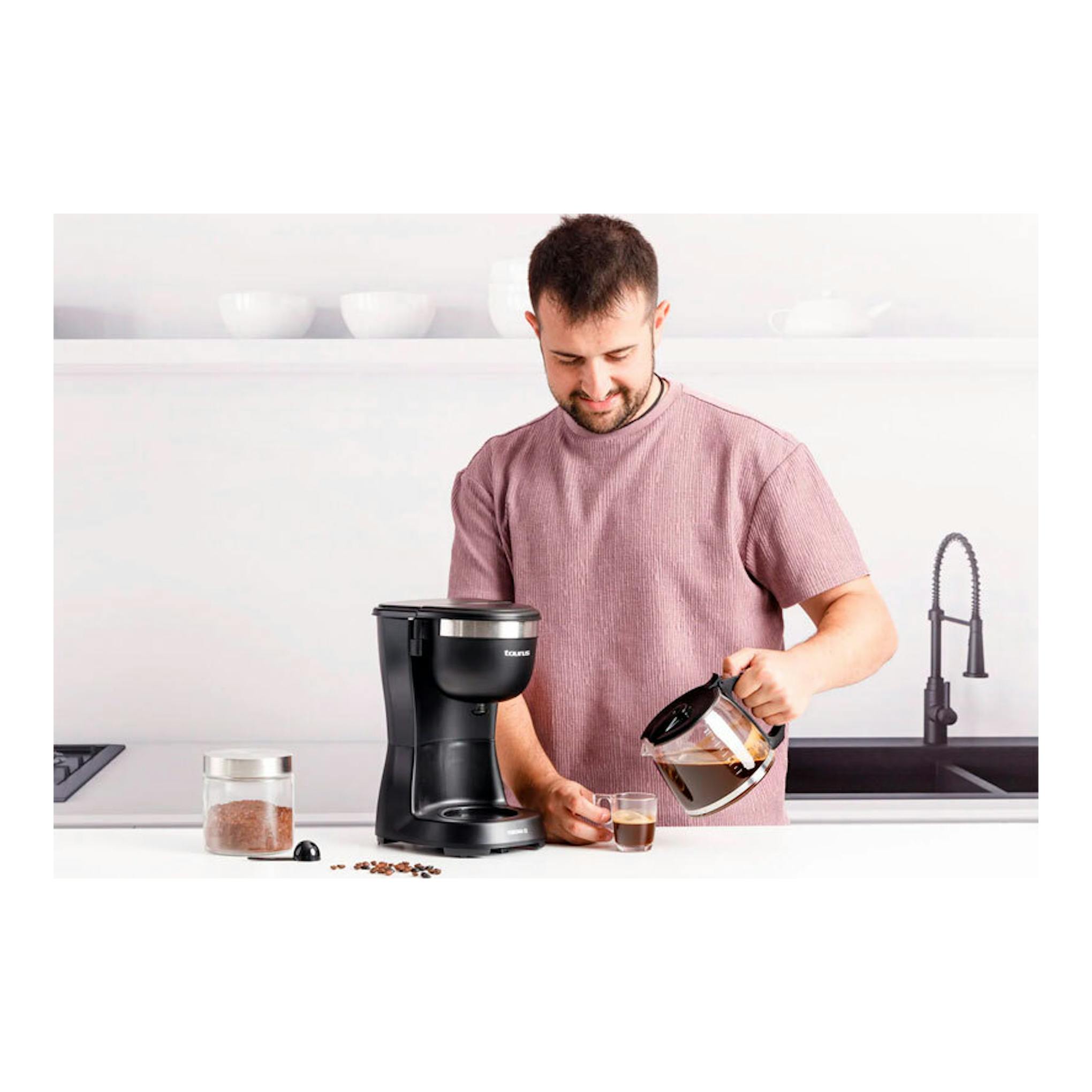 Cafetera de goteo Taurus Verona 12 negra en una cocina, junto a un hombre sirviendo café.