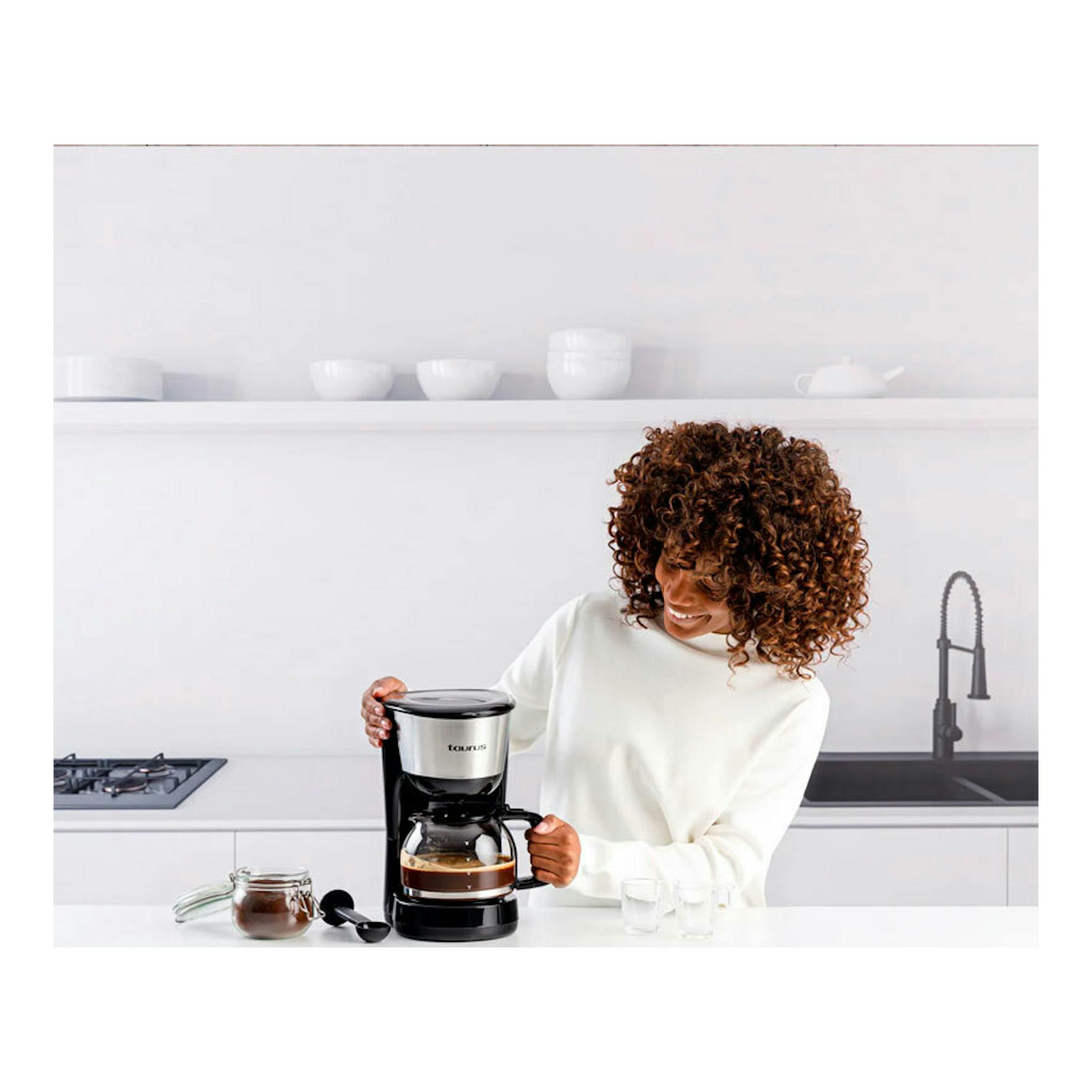 Cafetera de goteo Taurus Verona 12 Inox negra y plata, vista frontal, con una mujer sirviendo café.