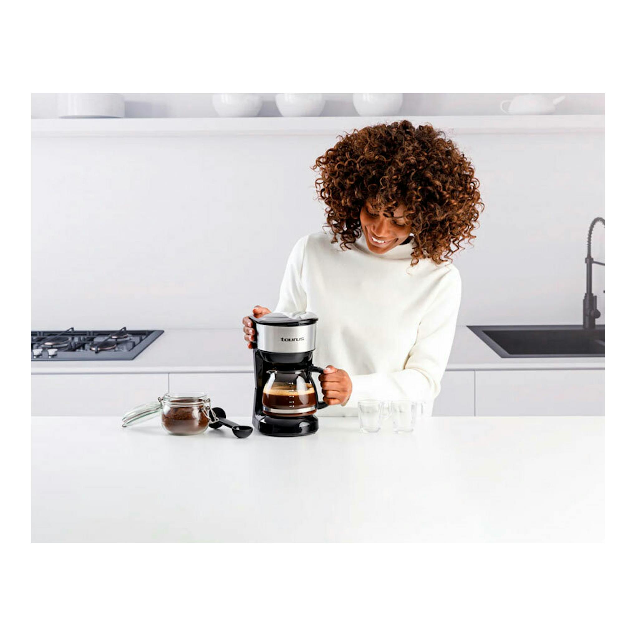 Vista frontal de una mujer con cafetera de goteo Taurus Verona 6 Inox negra y acero.