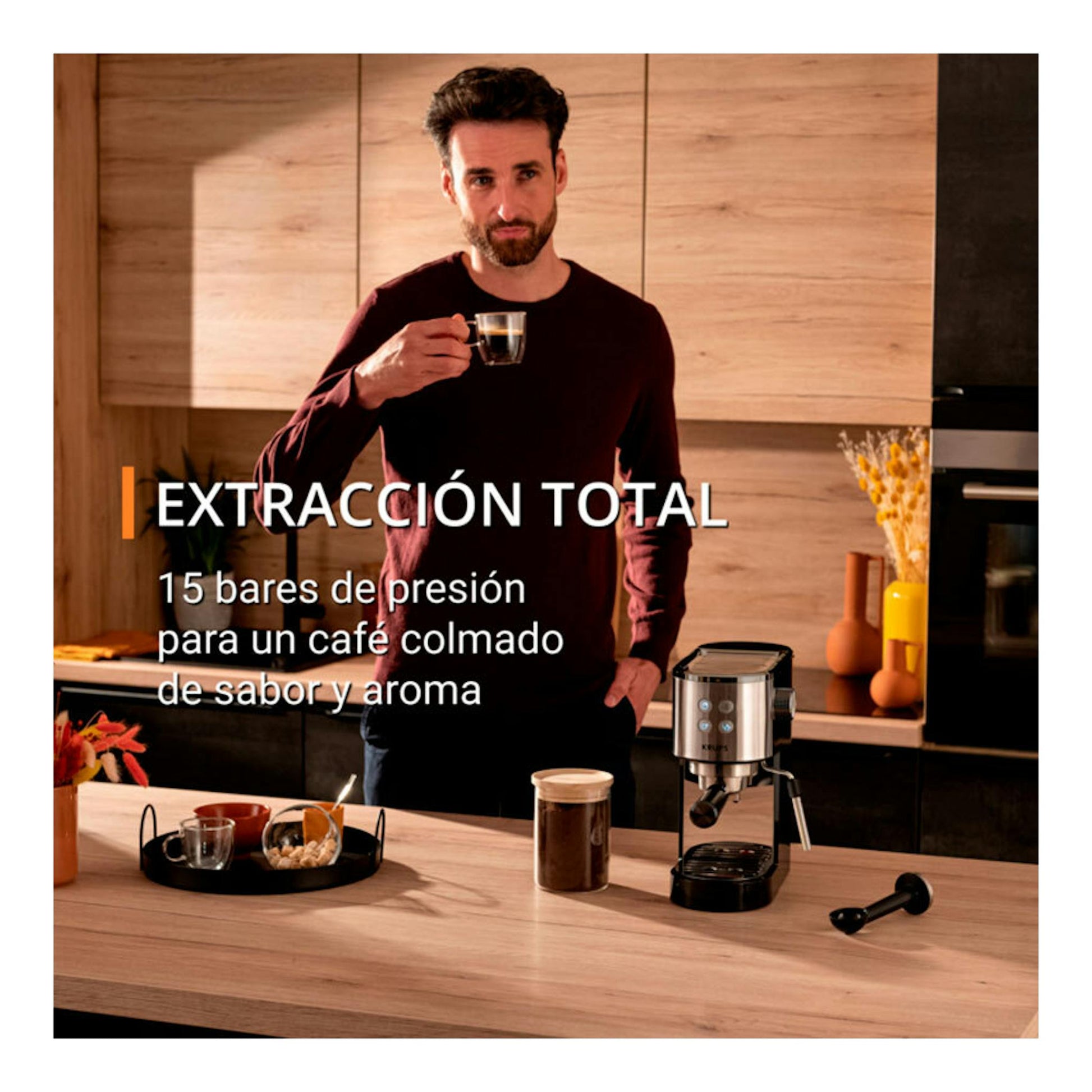 Cafetera espresso Krups XP444C10 de acero inoxidable, vista frontal en una cocina con un hombre al fondo.