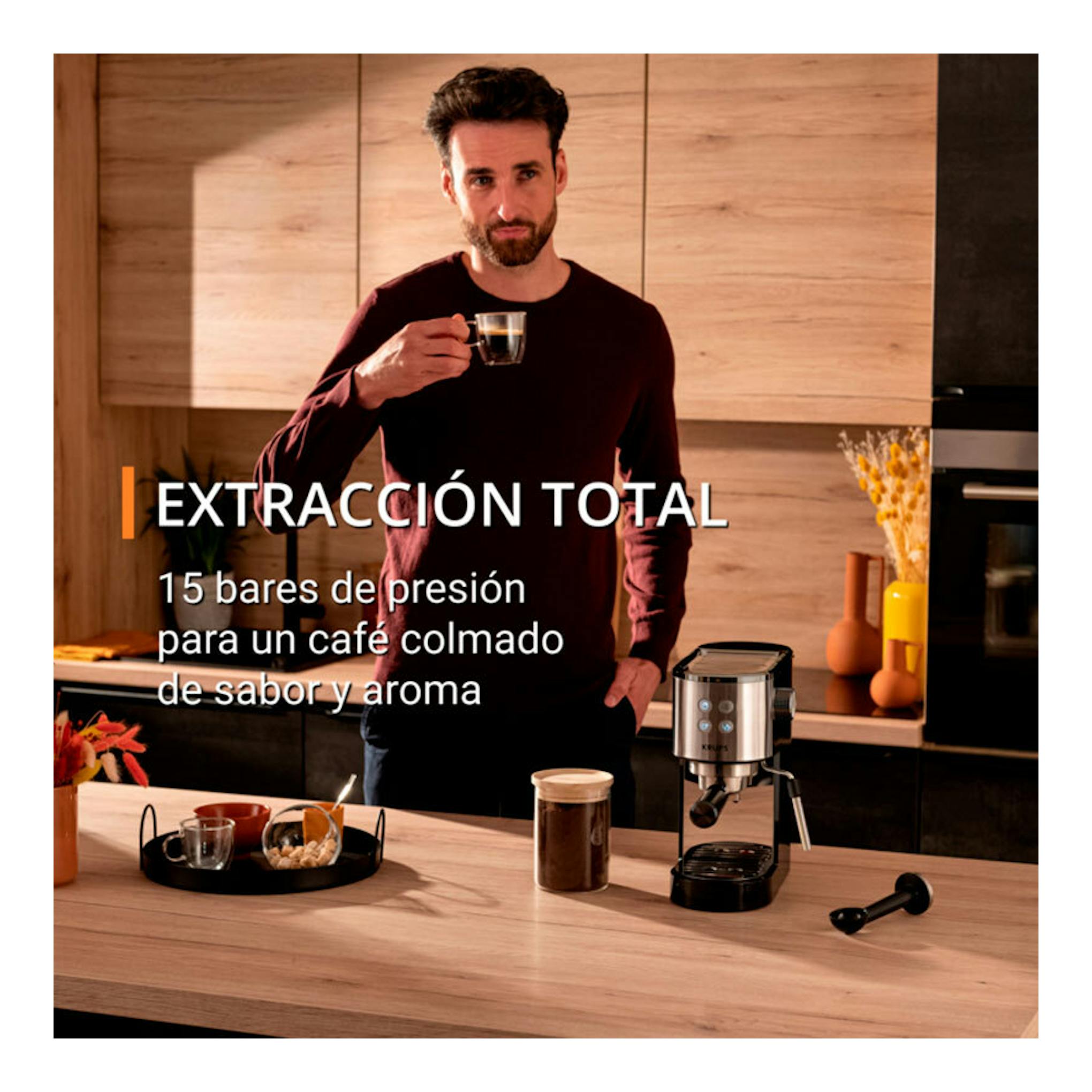 Cafetera espresso Krups XP444C10 de acero inoxidable, vista frontal en una cocina con un hombre al fondo.