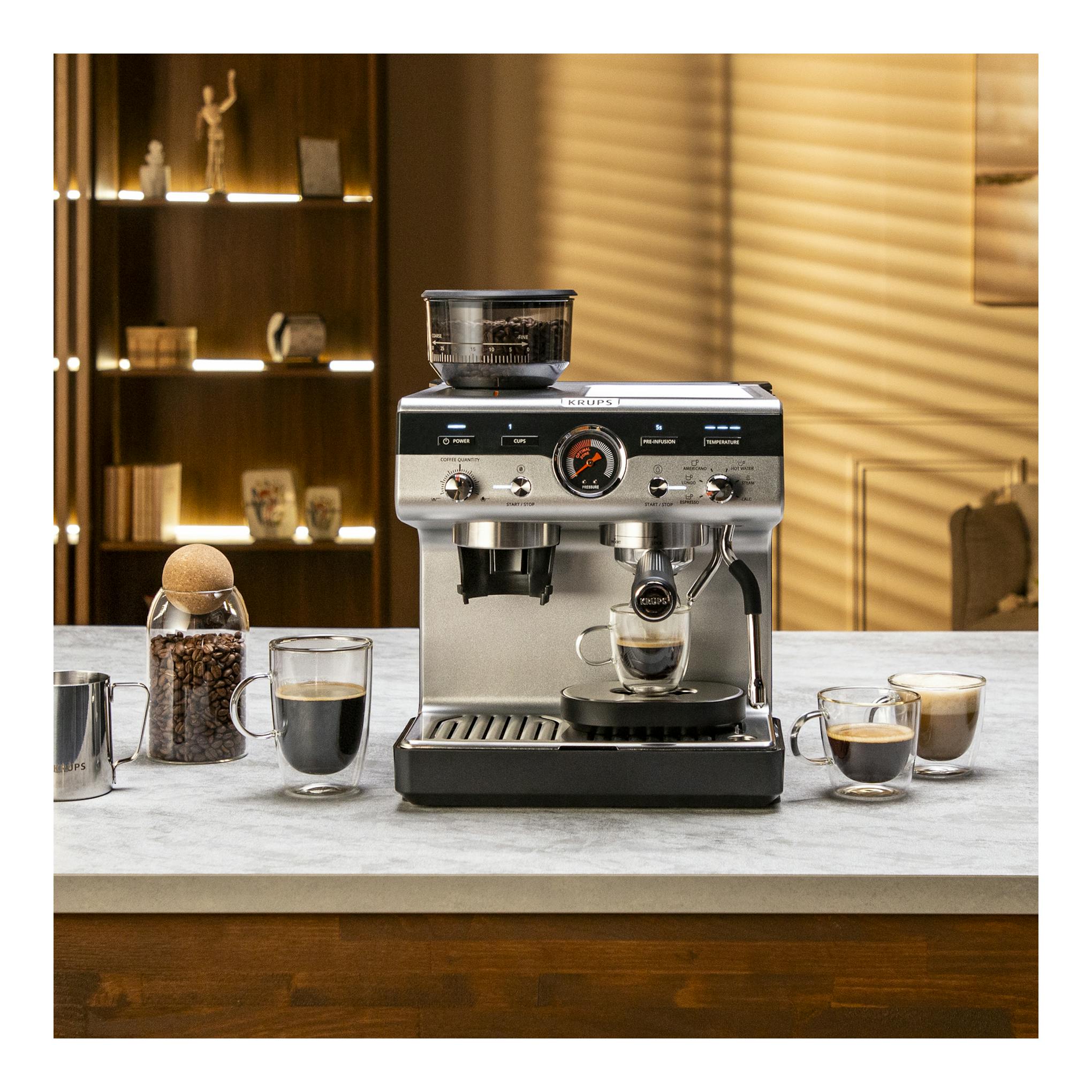 Cafetera espresso Krups XP801T10 plateada, vista frontal, con molinillo integrado y taza bajo el grupo.