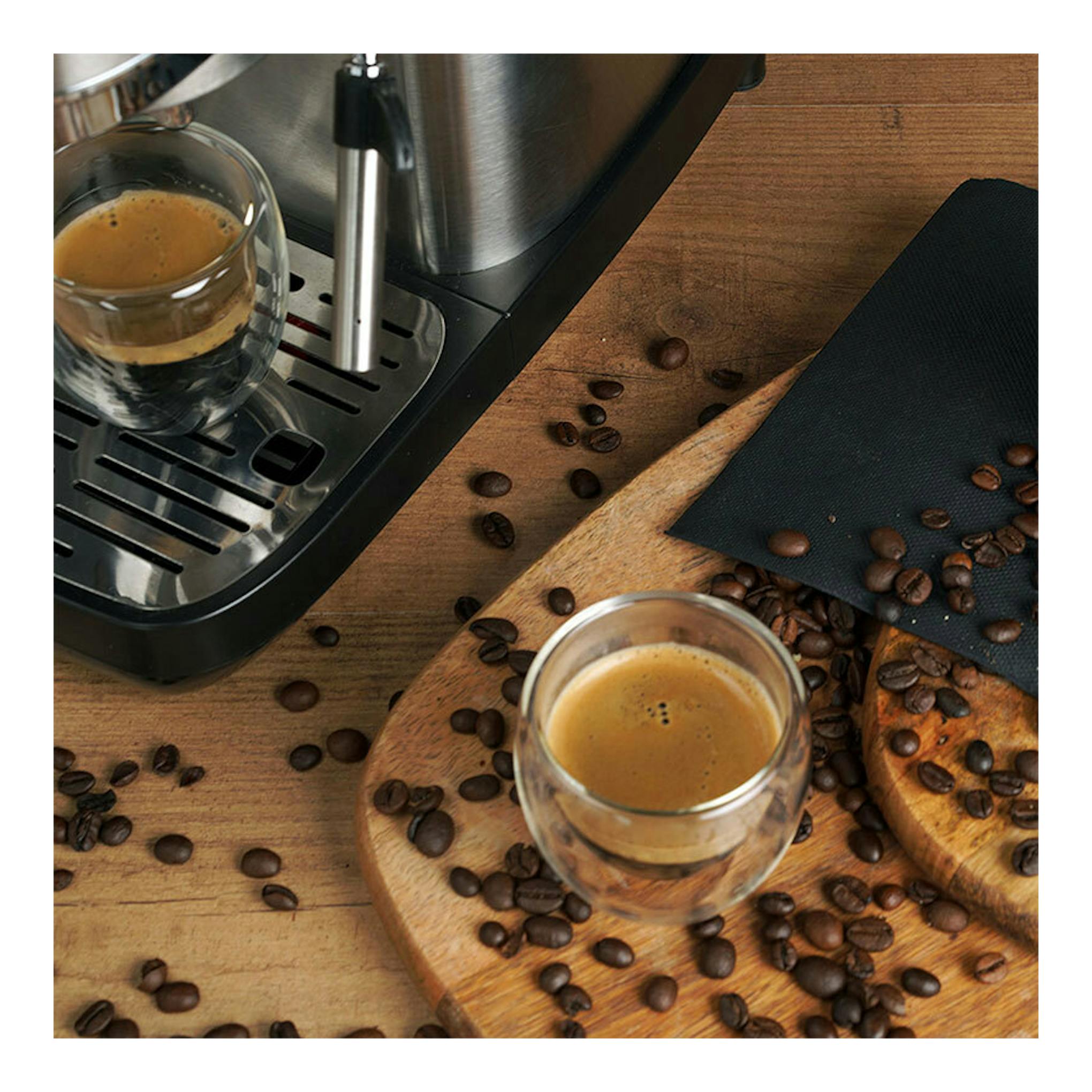 Cafetera espresso Ariete Slim de metal, vista parcial en ángulo, con dos tazas de café y granos sobre mesa de madera.