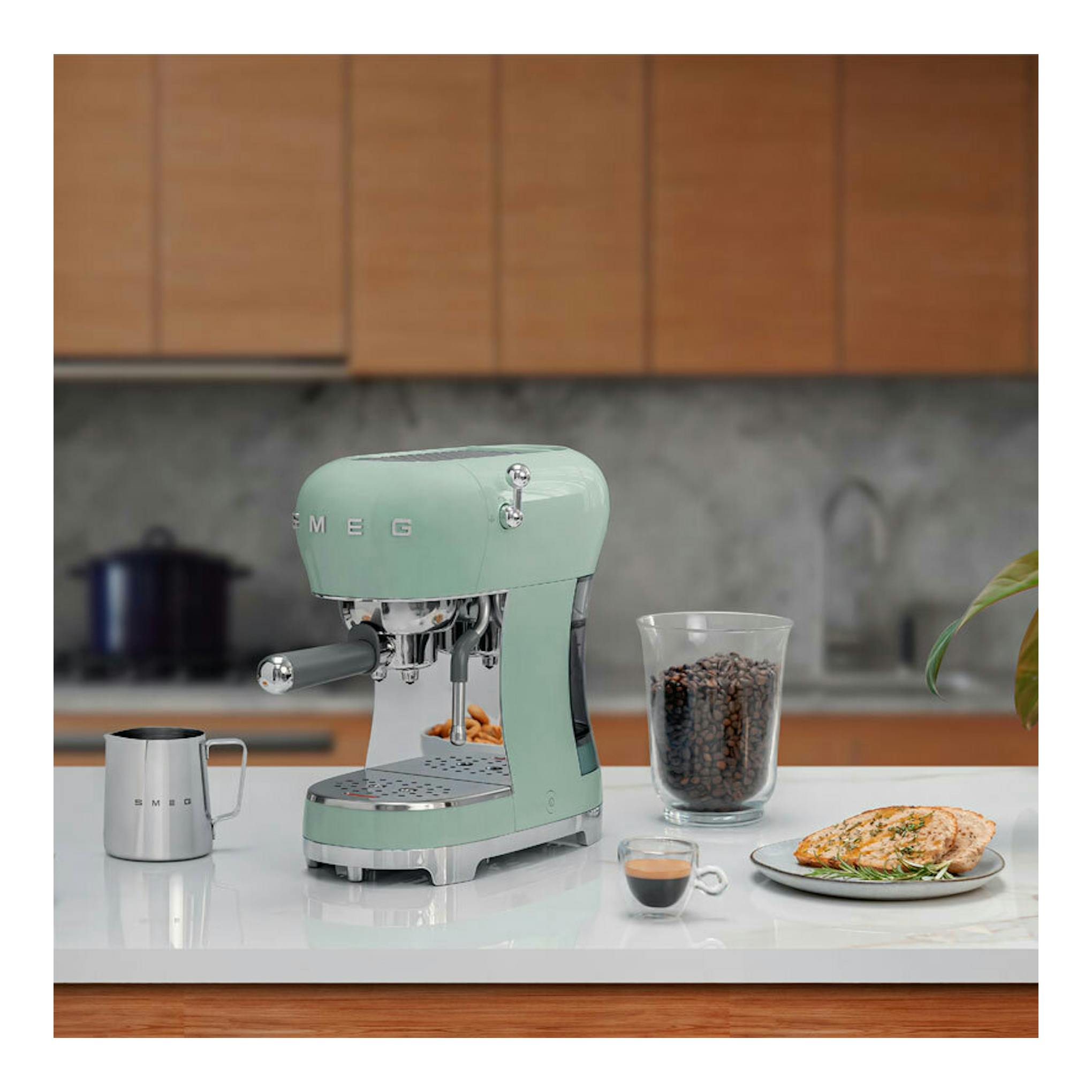 Cafetera espresso Smeg ECF02PGEU verde menta, vista frontal en encimera con taza, café y plato.