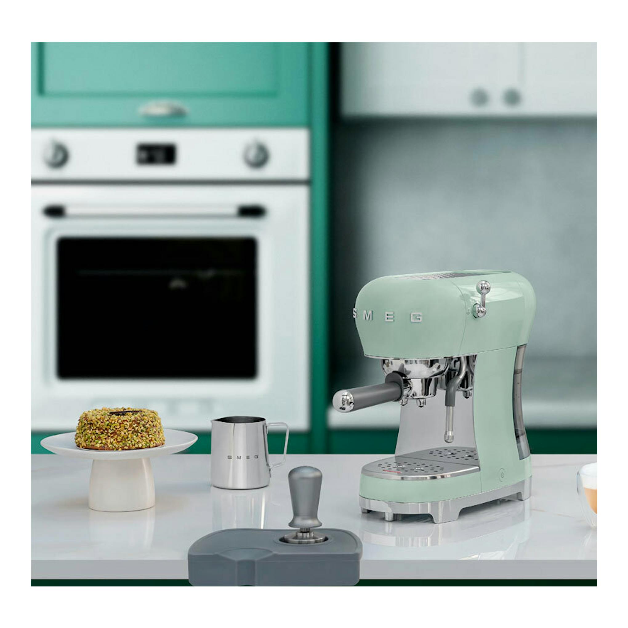 Cafetera expreso Smeg ECF02PGEU verde menta, vista frontal lateral sobre encimera en una cocina.