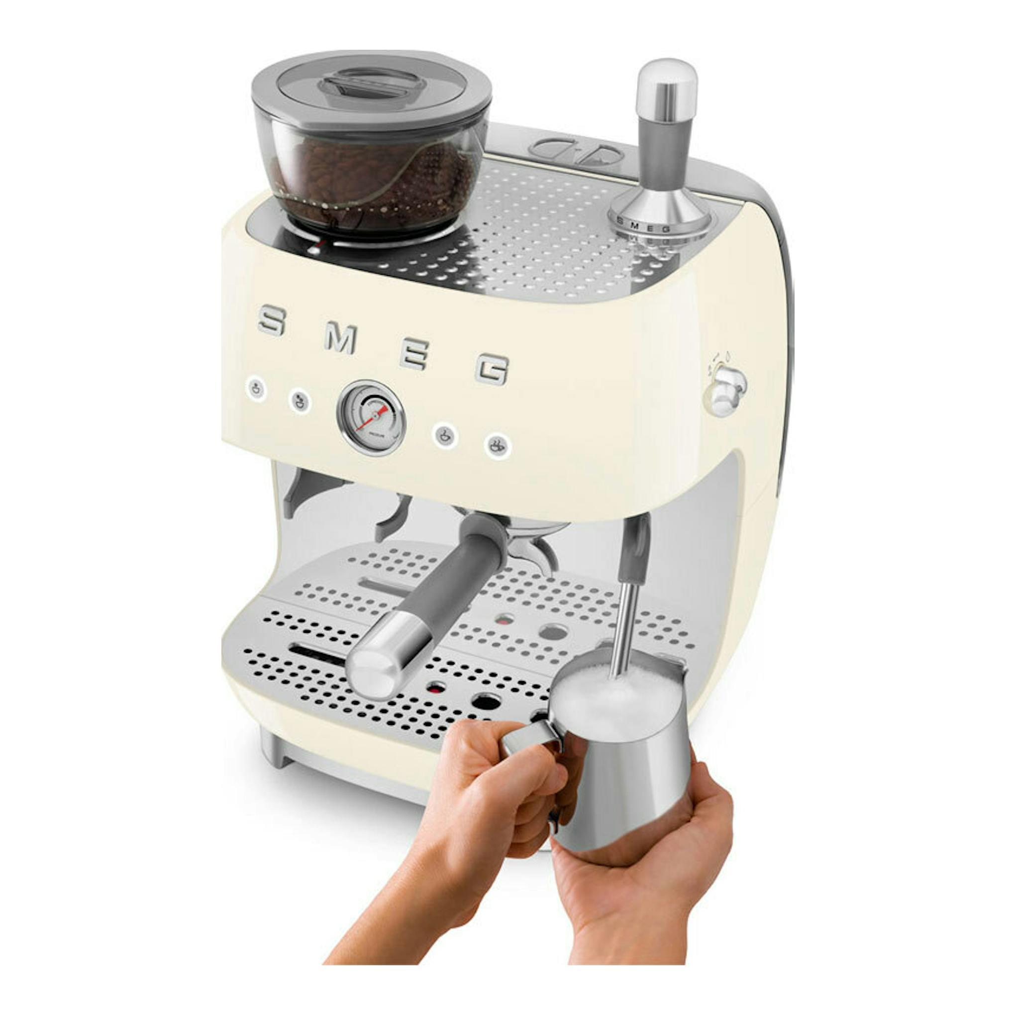 Cafetera espresso Smeg EGF03CREU crema, vista frontal tres cuartos, con molinillo y manos espumando leche.