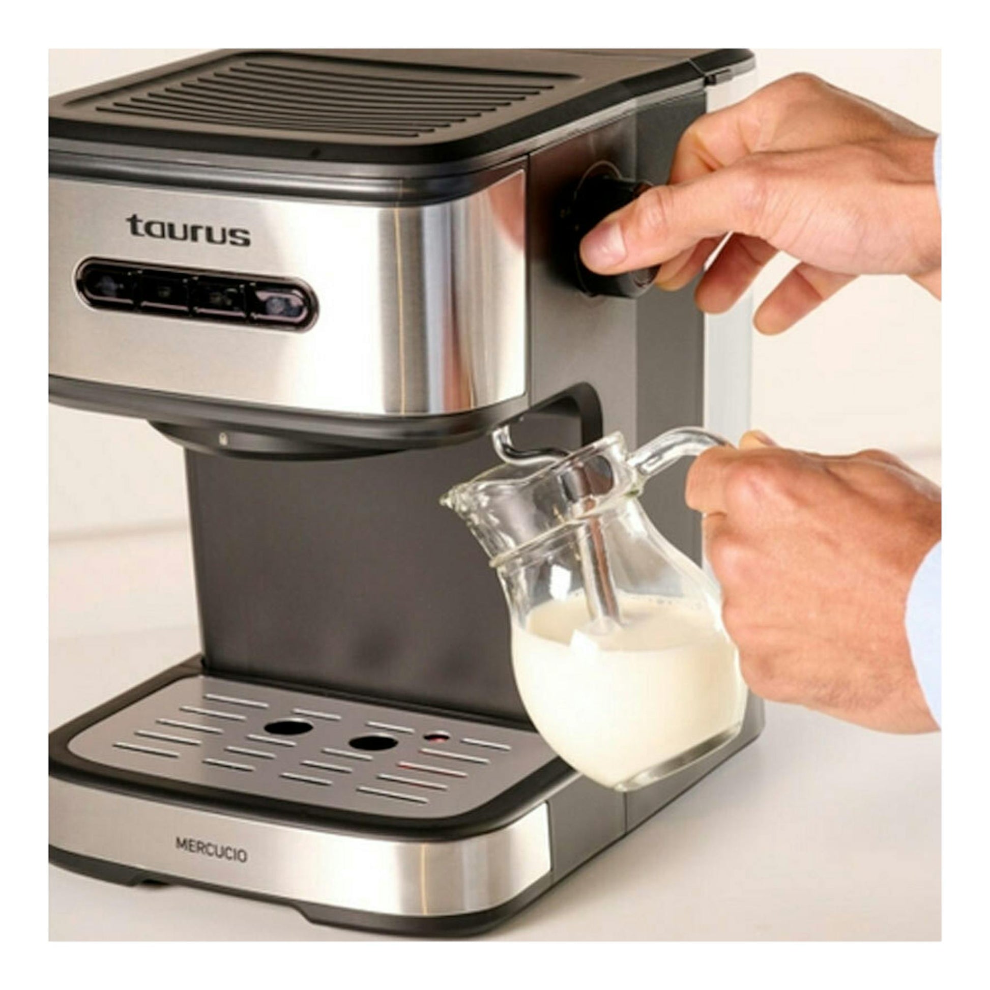 Cafetera expreso Taurus Mercucio, vista frontal en ángulo, color plata y negro, con manos usando jarra de leche.