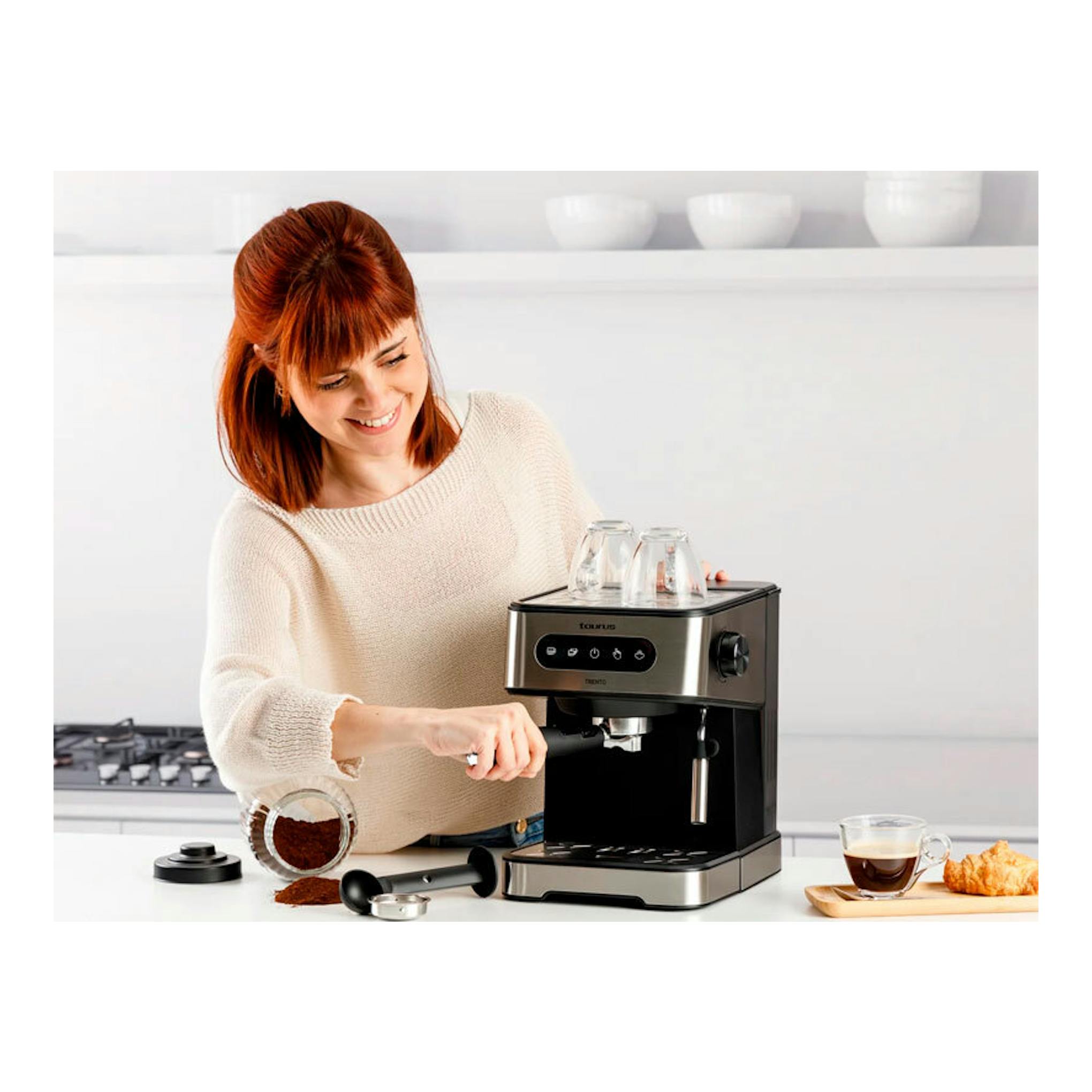 Cafetera espresso Taurus Trento negra y acero, vista frontal, con una mujer preparando café.