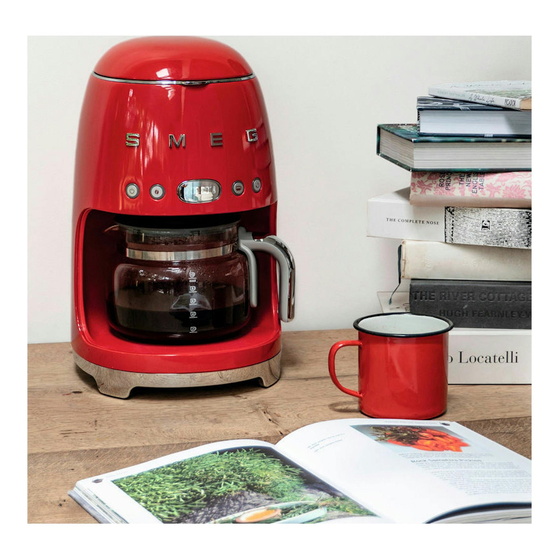 Cafetera de goteo Smeg DCF02 roja, vista frontal sobre una mesa, con taza roja.