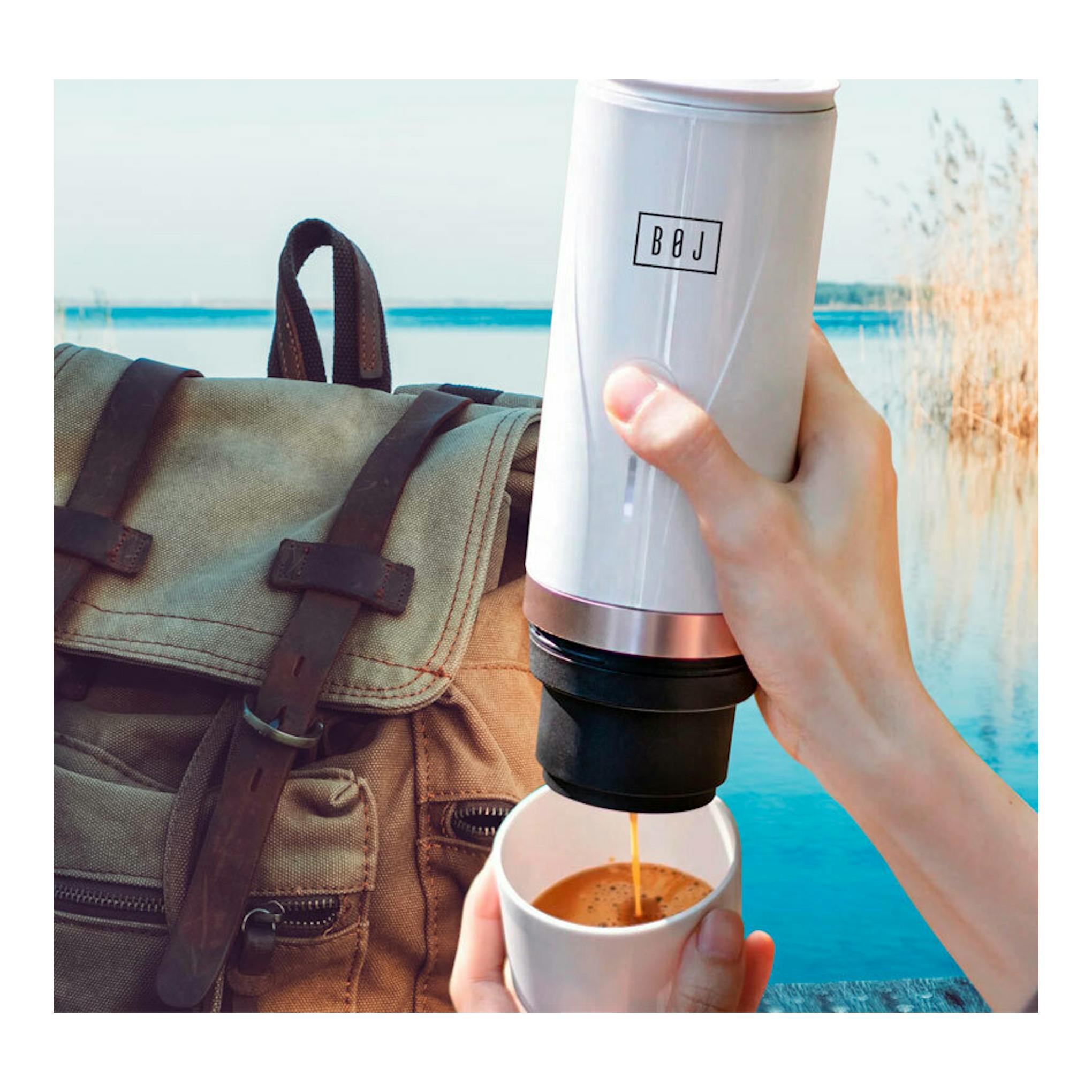 Cafetera portátil BOJ Giro blanca, vista frontal, vertiendo café en una taza junto a una mochila.