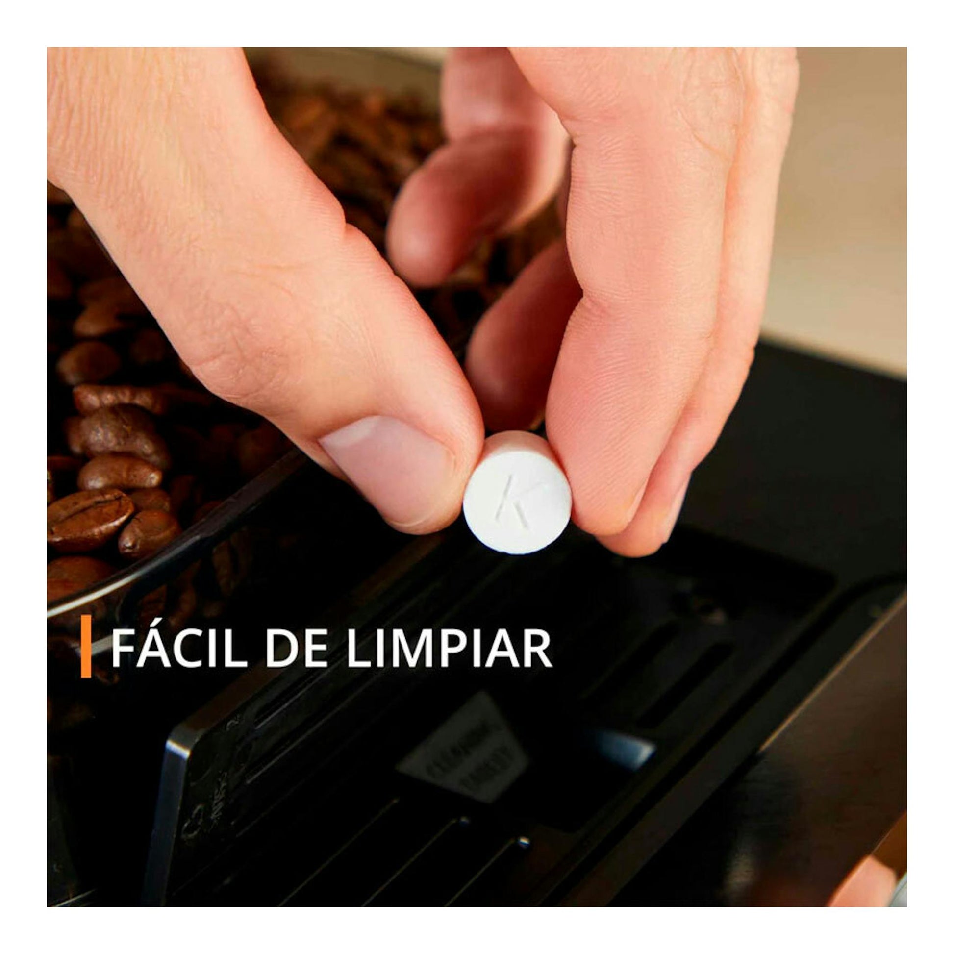 Krups EA910A10, primer plano de manos colocando una pastilla en el compartimento de una cafetera negra con café en grano.