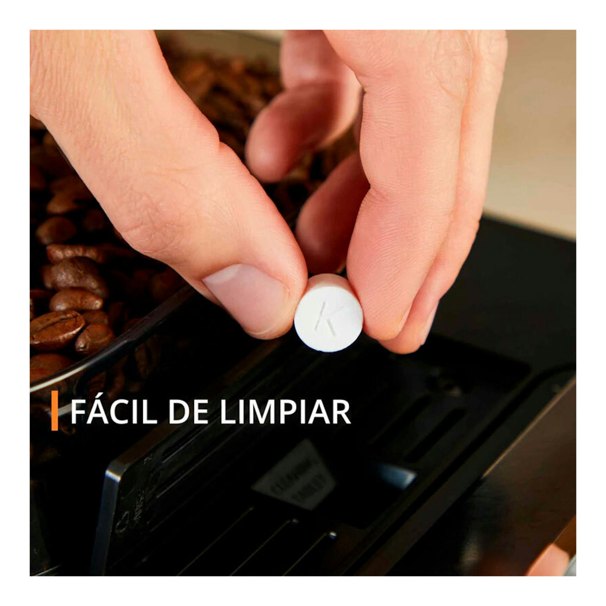 Krups EA910A10, primer plano de manos colocando una pastilla en el compartimento de una cafetera negra con café en grano.
