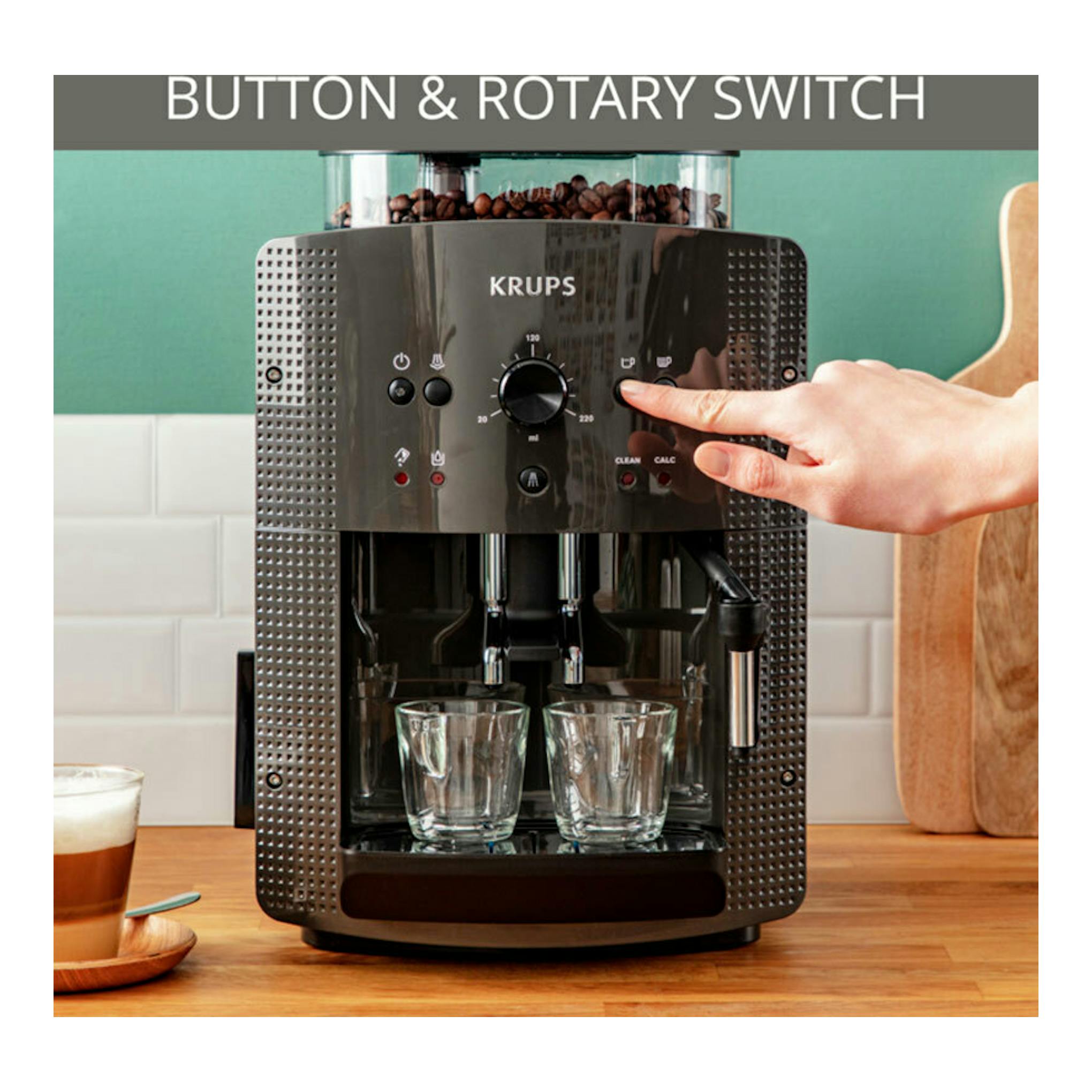 Cafetera automática Krups EA810B70 negra, vista frontal, con una mano pulsando un botón y dos vasos debajo.