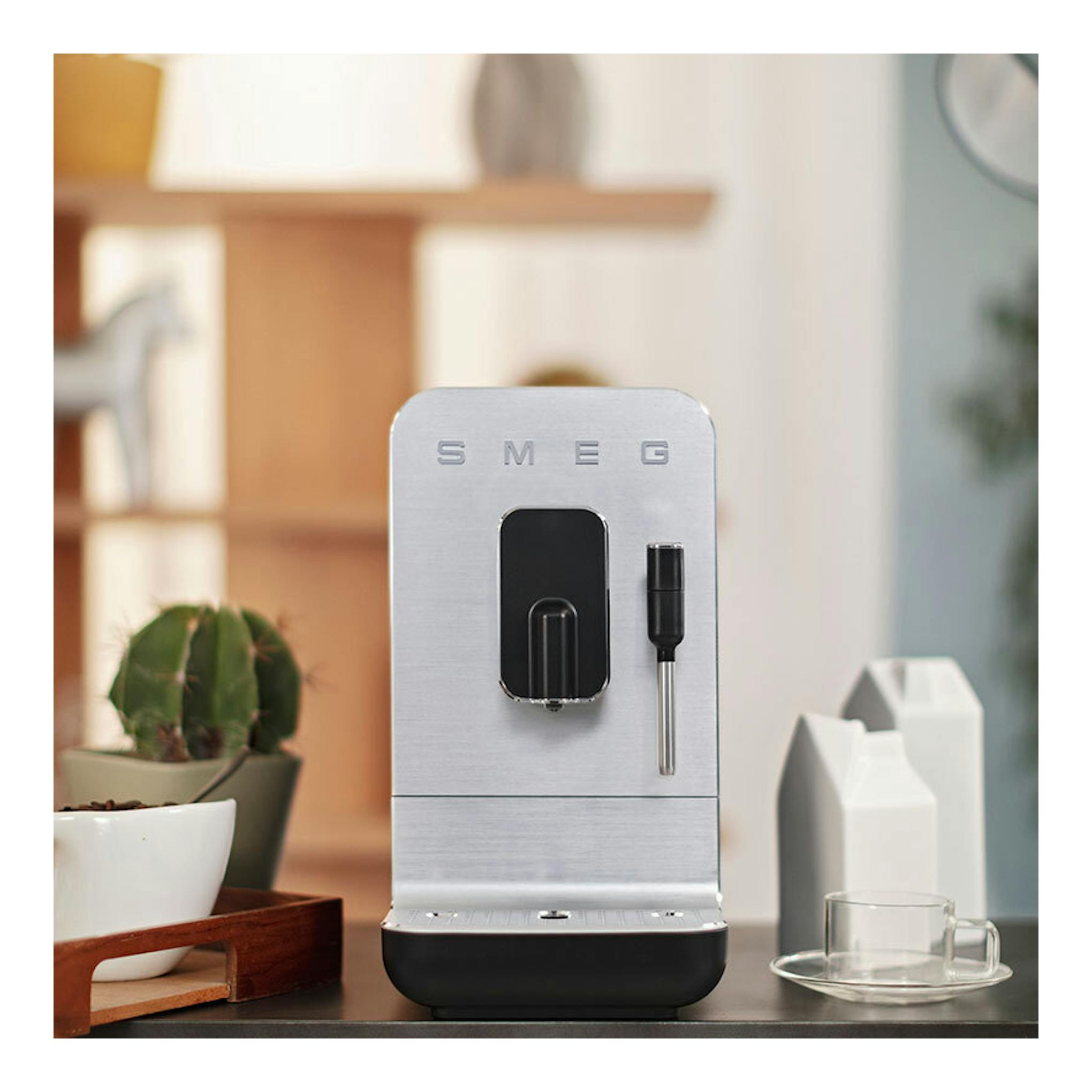 Cafetera superautomática Smeg BCC12BLMEU, vista frontal, en acero inoxidable con base negra.
