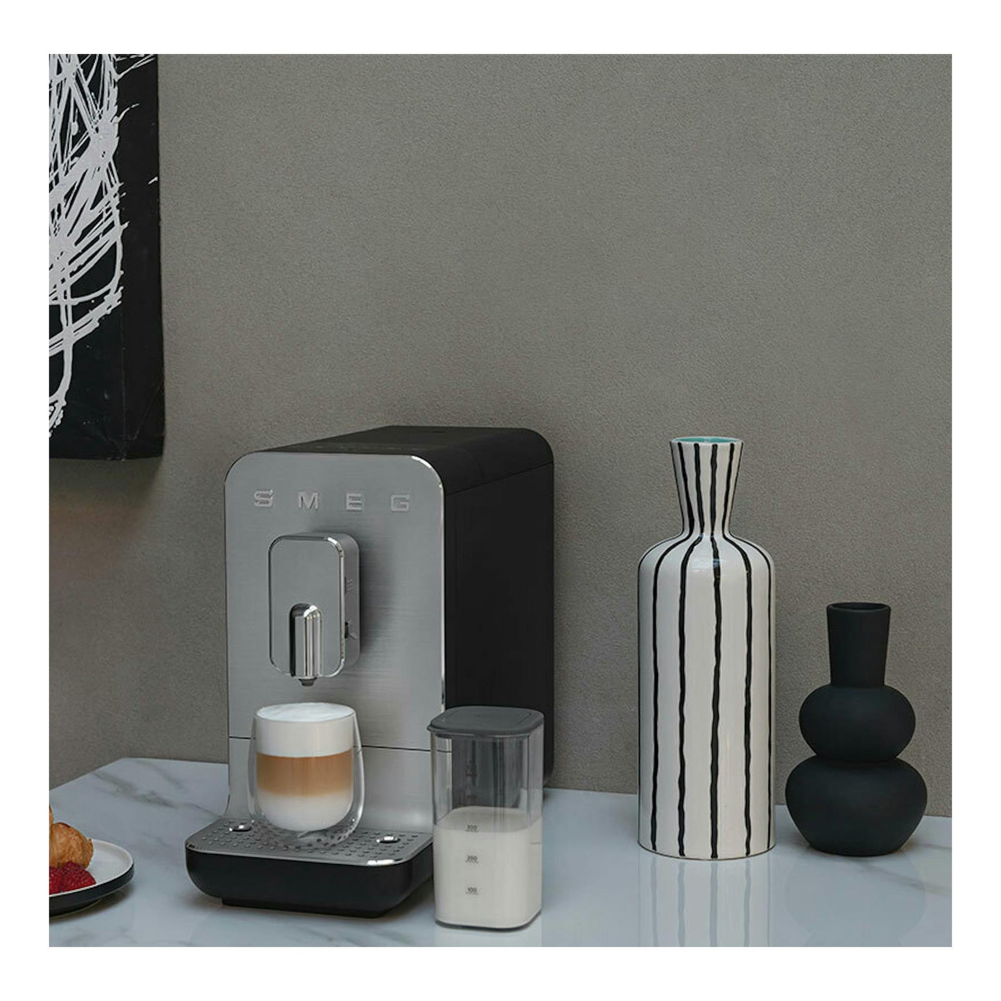 Cafetera superautomática Smeg BCC13BLMEU negra, vista frontal, con taza y recipiente de leche.